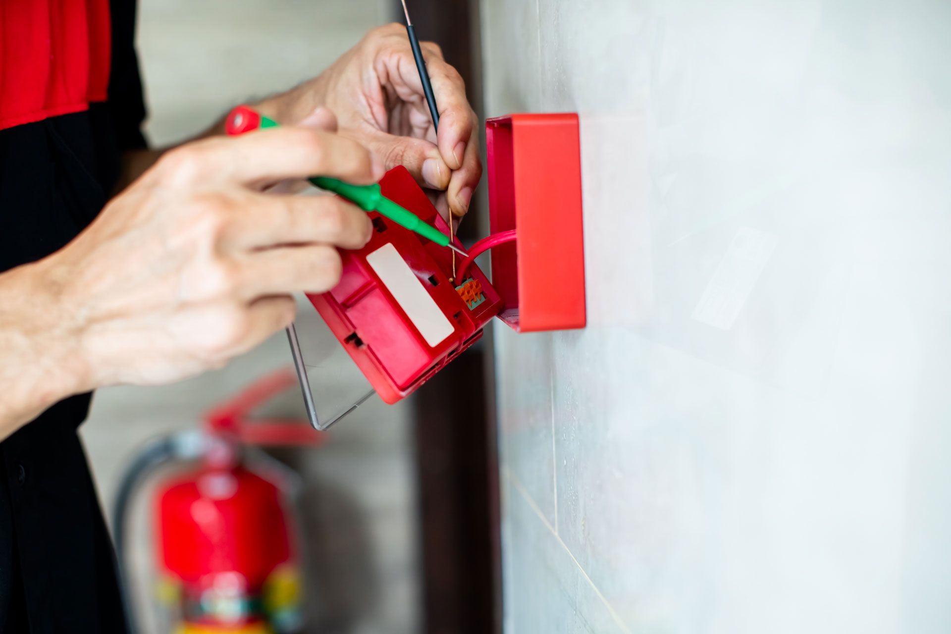 Hands wiring a red wall-mounted electrical box with a screwdriver