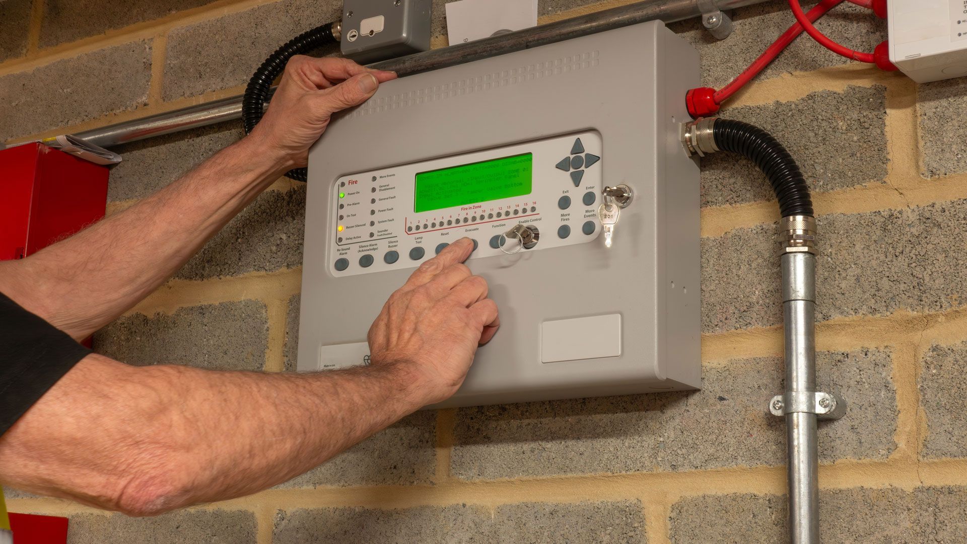 Person adjusting a wall-mounted control panel with a green display in a brick utility room