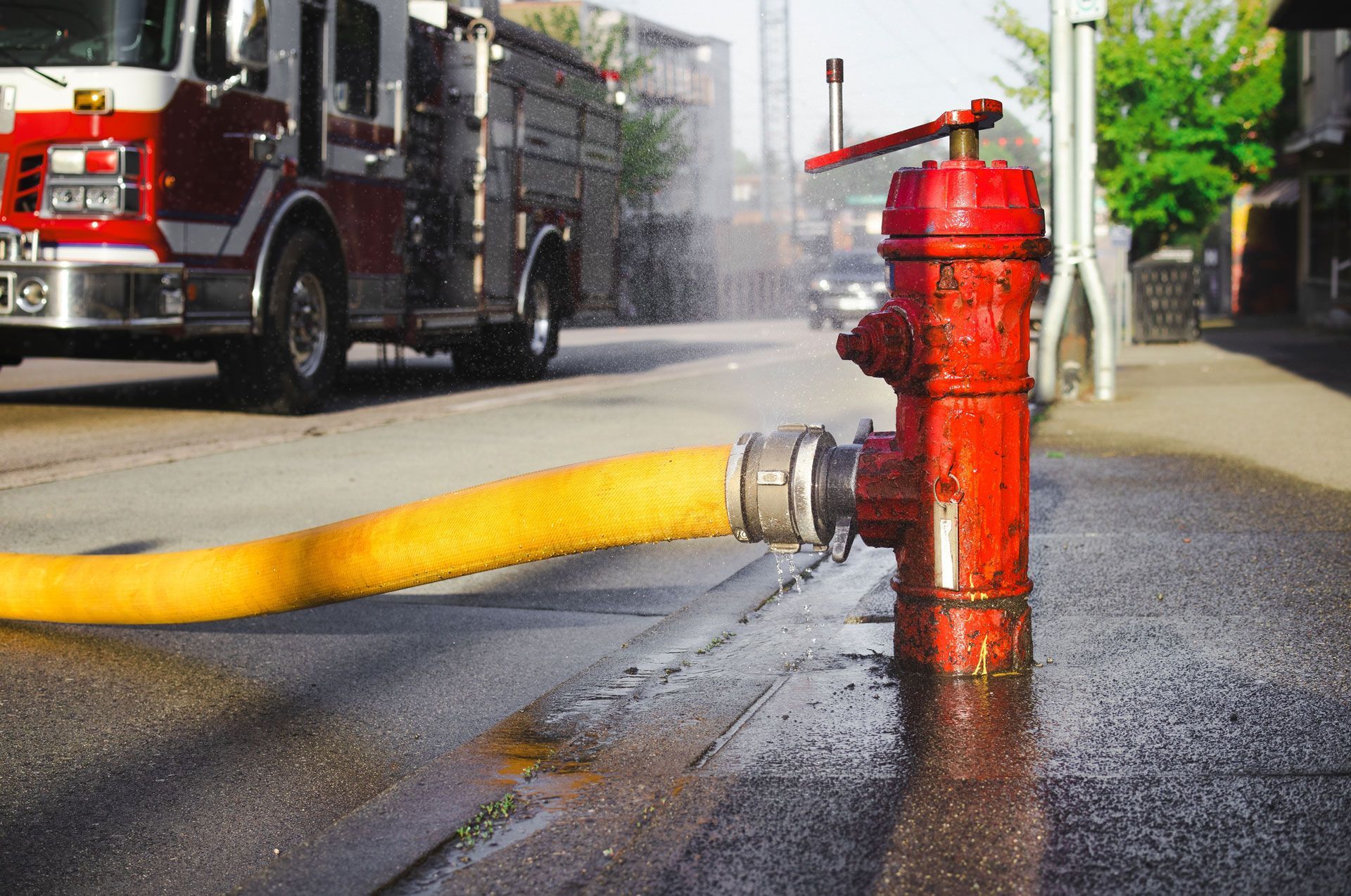 Fire truck connected to a red fire hydrant with a yellow hose spraying water on a wet street