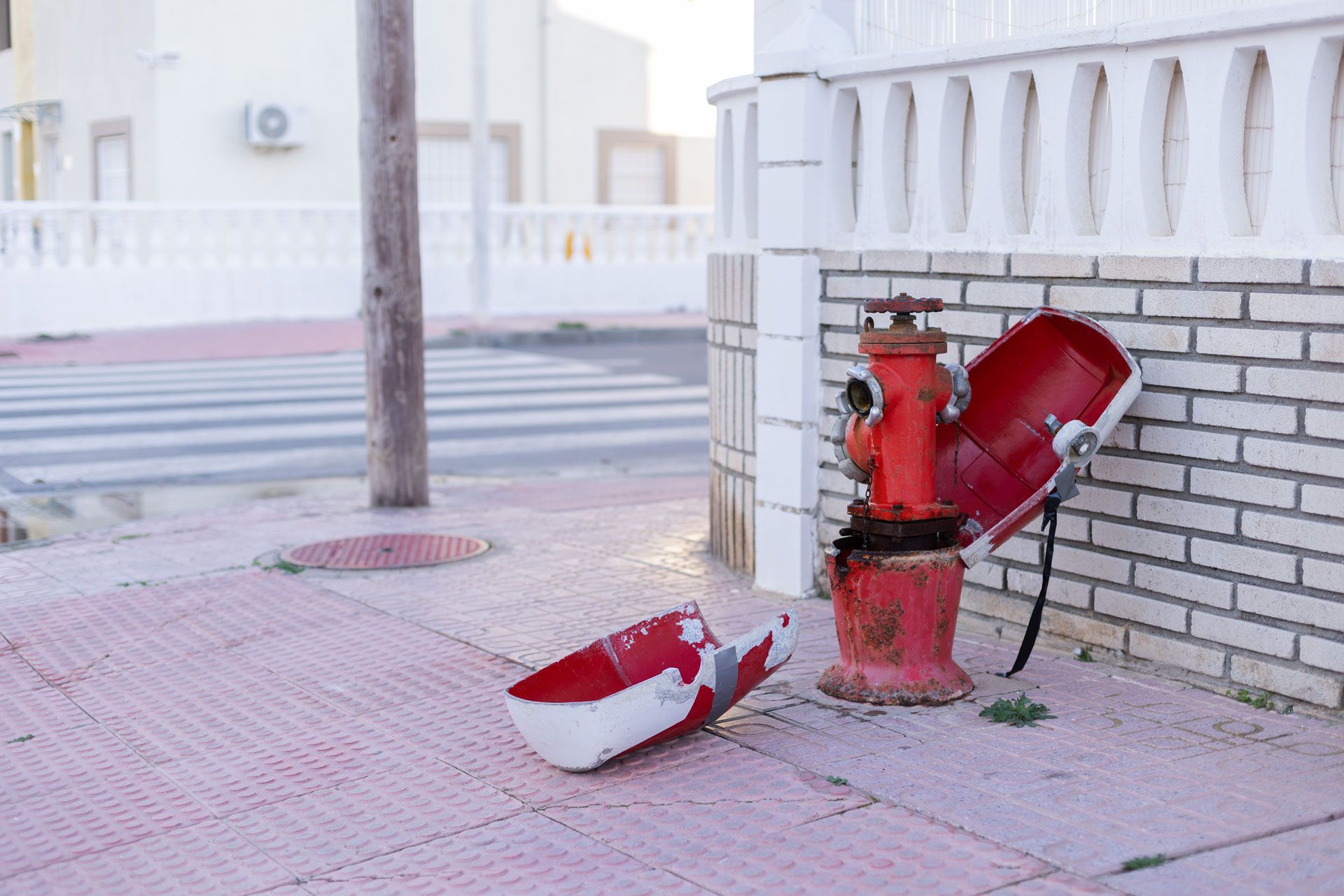 Red fire hydrant beside a brick wall, with a fallen red-and-white fire extinguisher on the sidewalk.