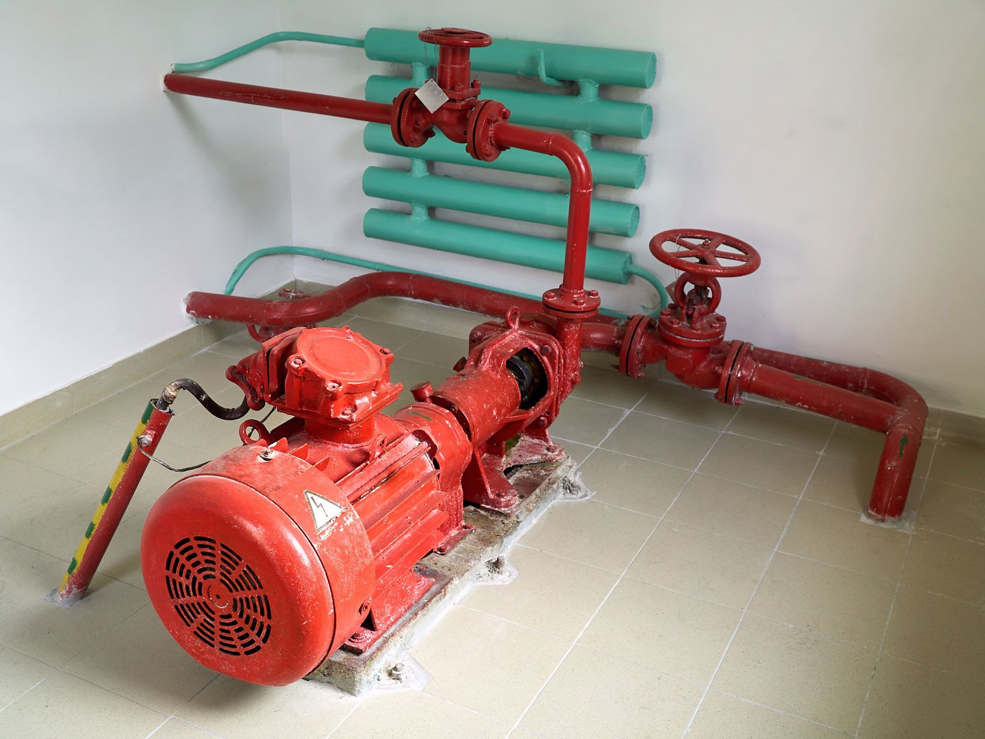 Red industrial pump and pipe system with red valves against a white wall