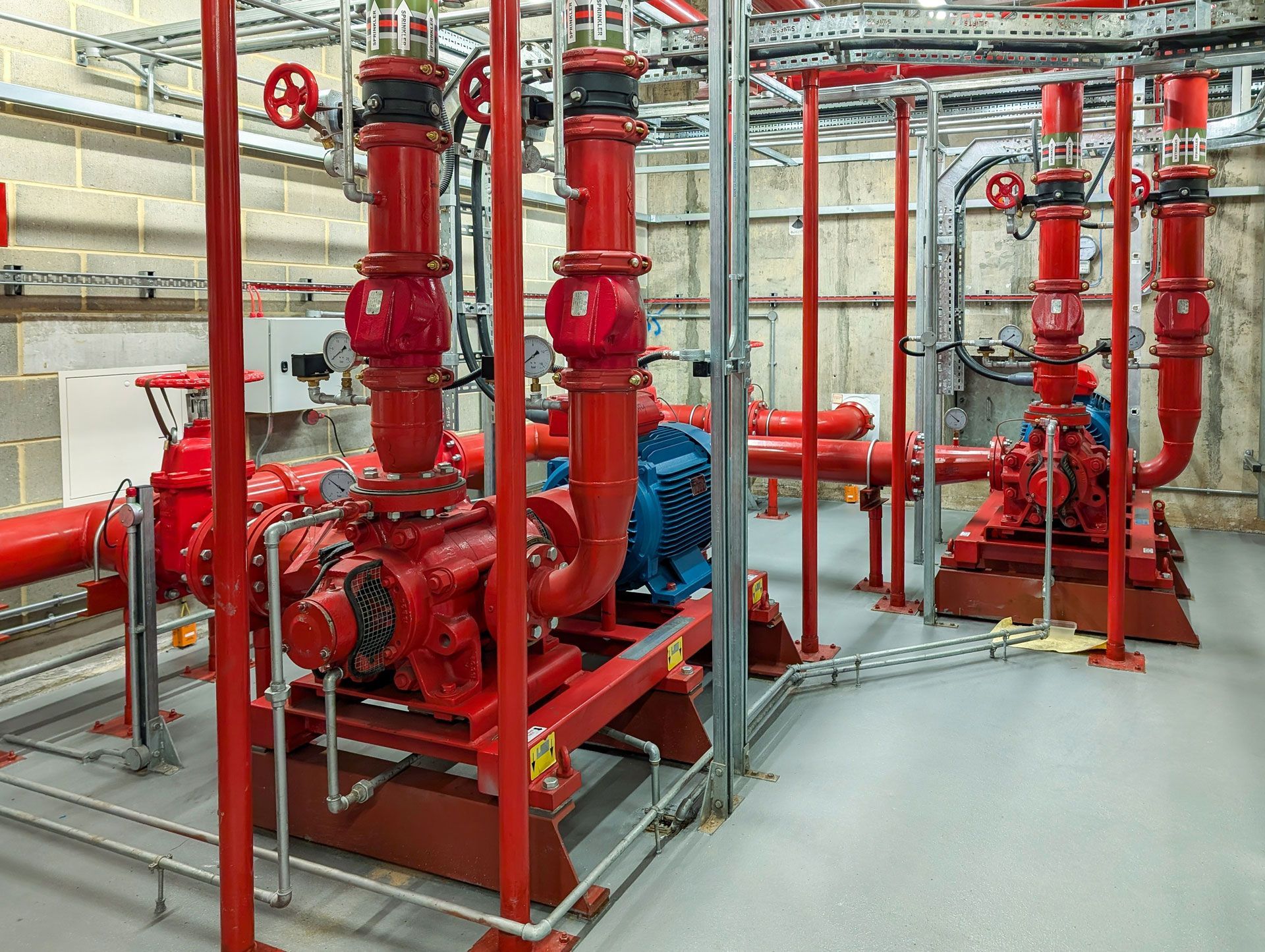 Red industrial pumps and pipes in a mechanical room with gray flooring and railings