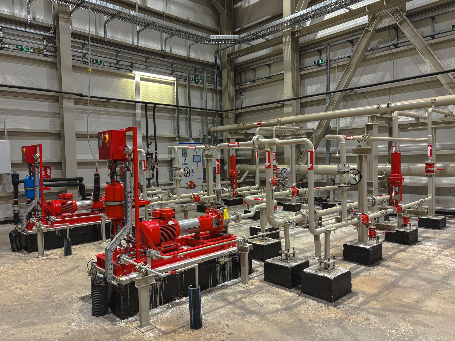 Industrial facility with red and silver piping, valves, and pumps on a concrete floor