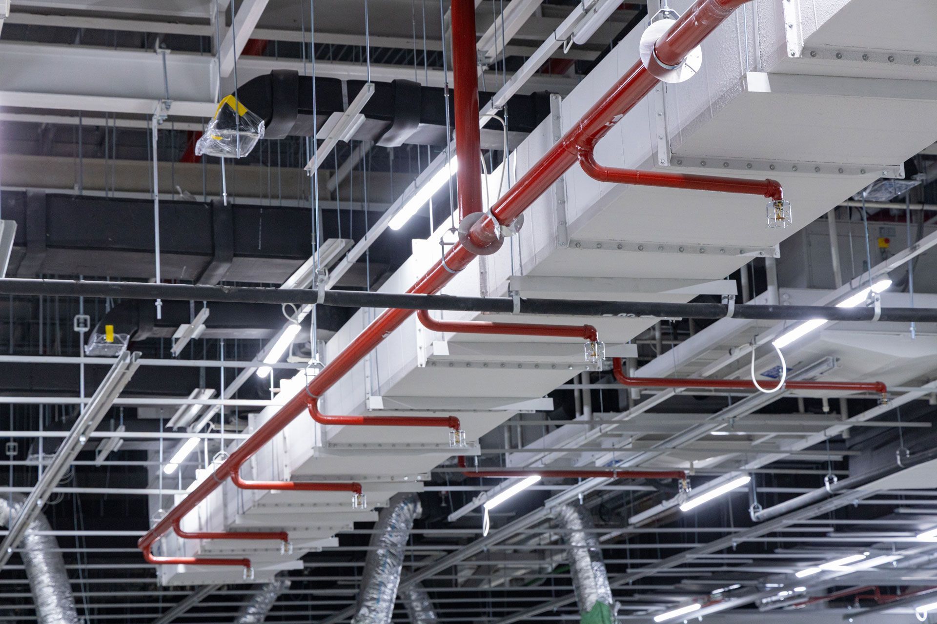 Industrial ceiling with exposed ducts, red pipes, and hanging lights in a large building interior