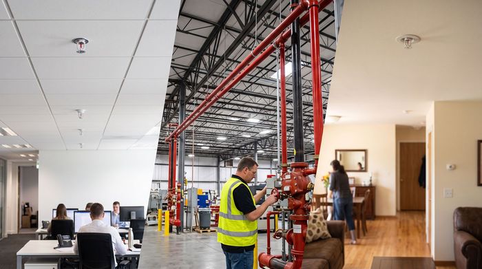 Office with exposed ceiling and red framework; workers in safety vests near a central staircase.