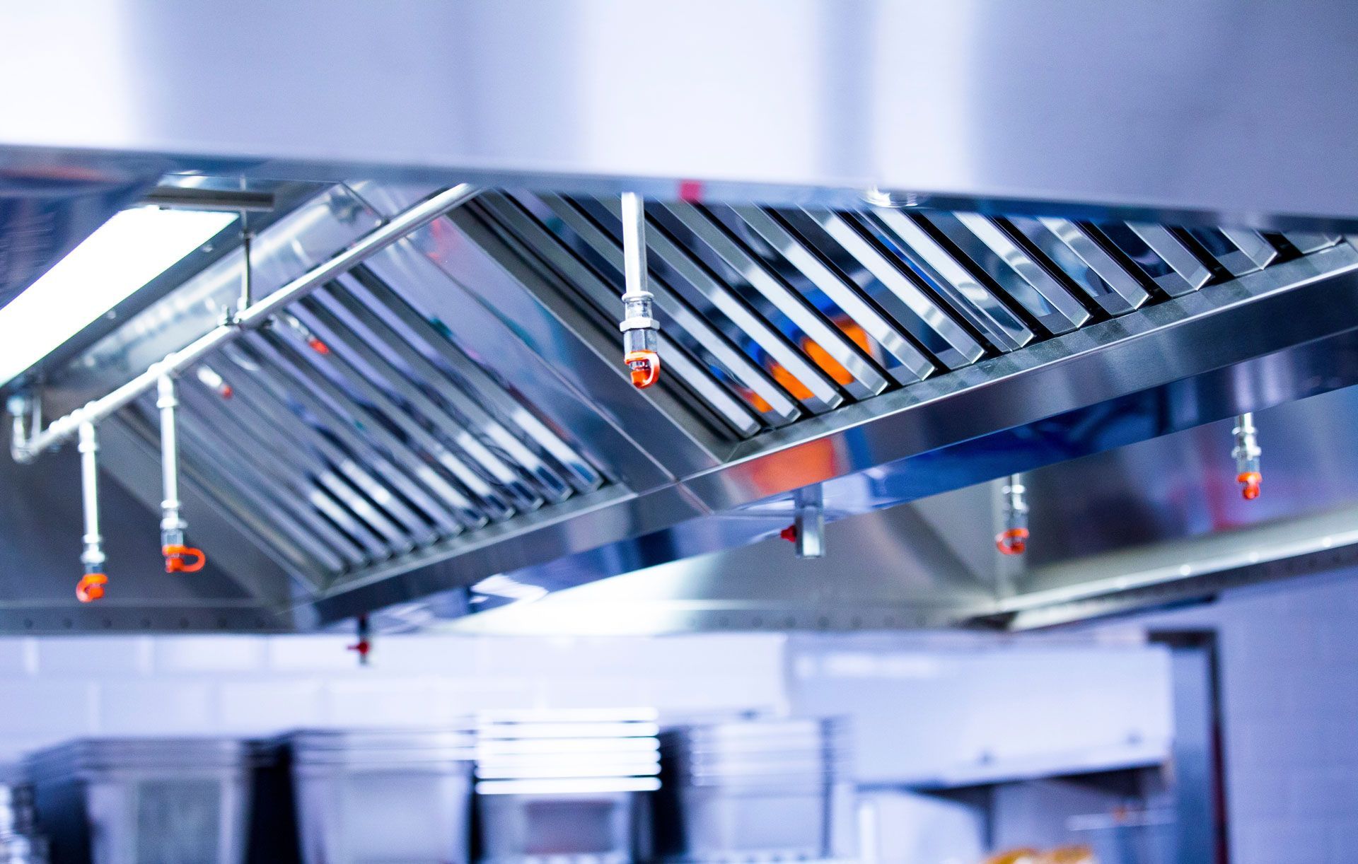 Stainless steel commercial kitchen hood with grease filters and hanging lights above cooking equipment