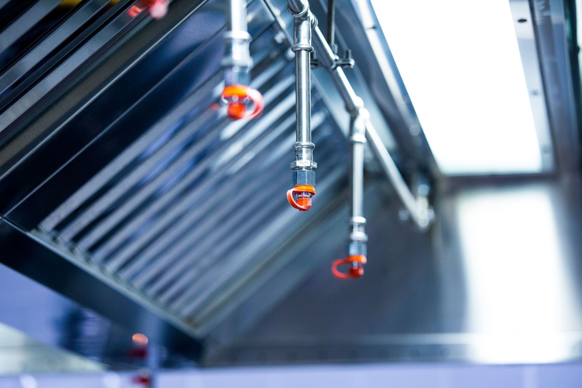 Stainless steel commercial kitchen hood with hanging sprinkler nozzles and red safety caps