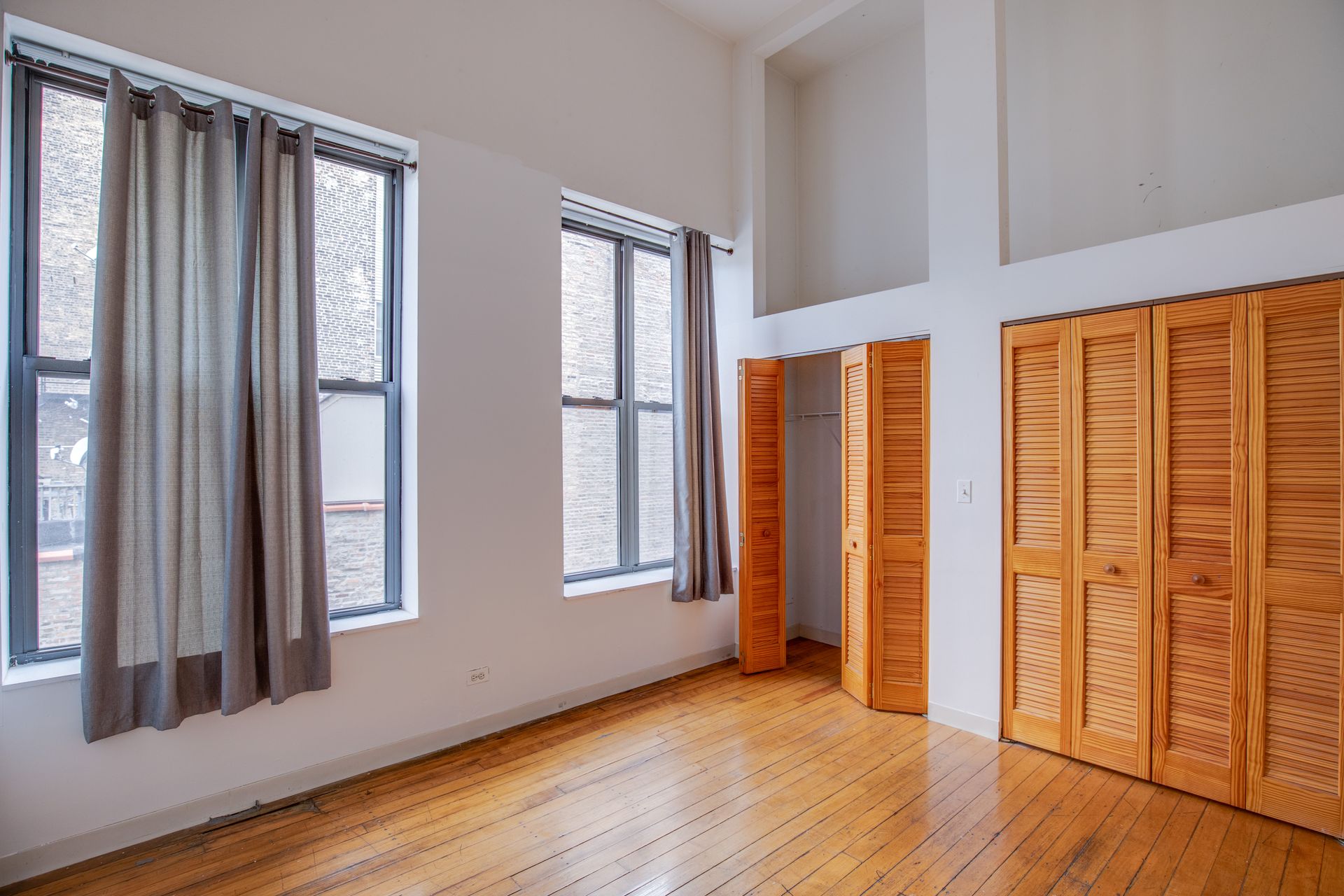 An empty bedroom with wooden floors and closets.