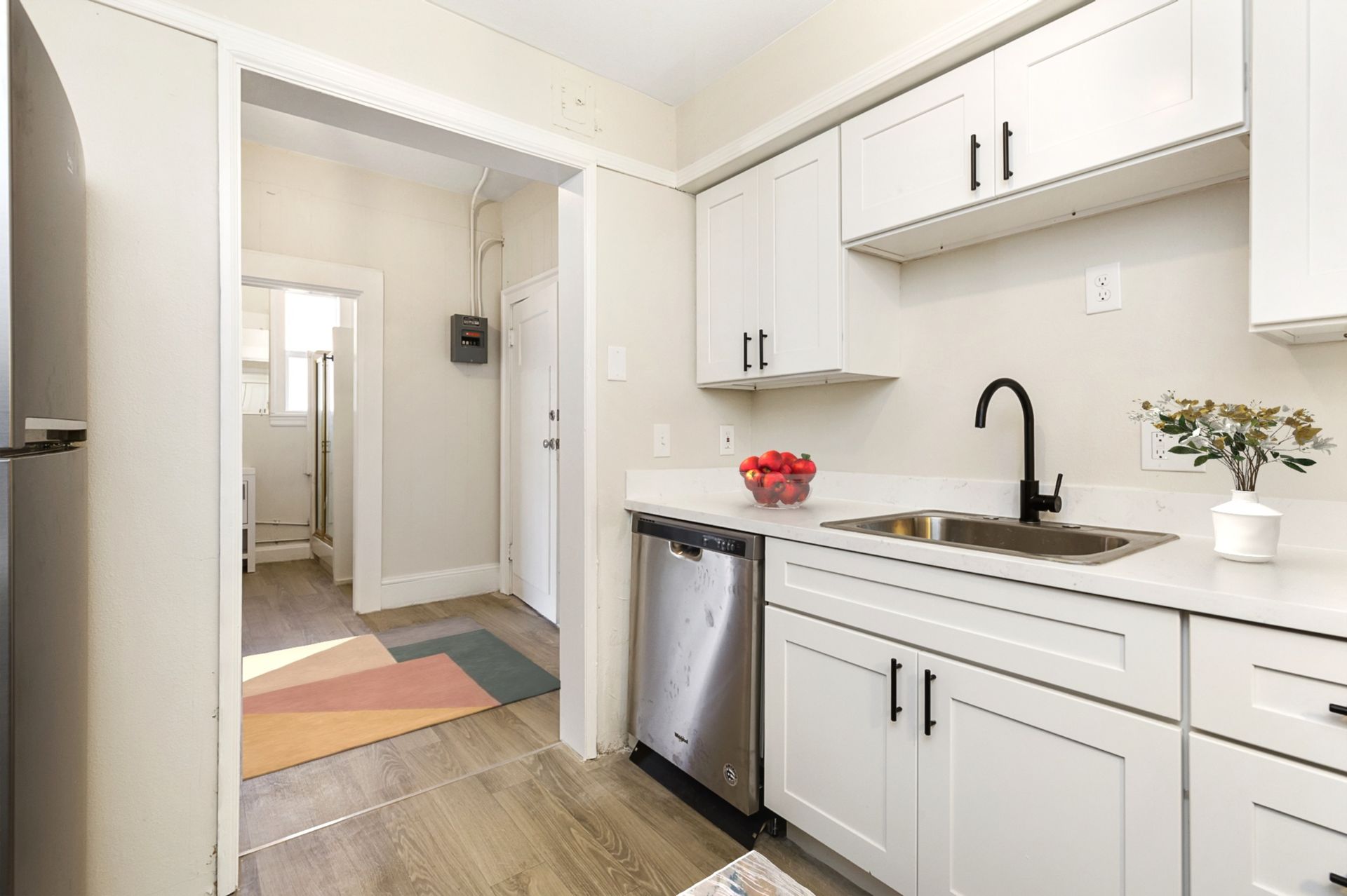 A kitchen with white cabinets , stainless steel appliances , a sink and a refrigerator.