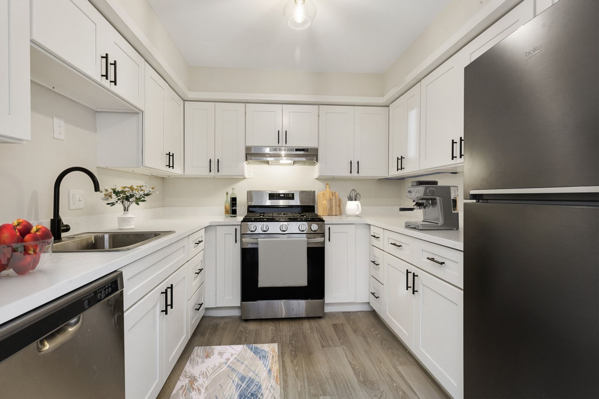 A kitchen with white cabinets , stainless steel appliances , a sink , and a refrigerator.
