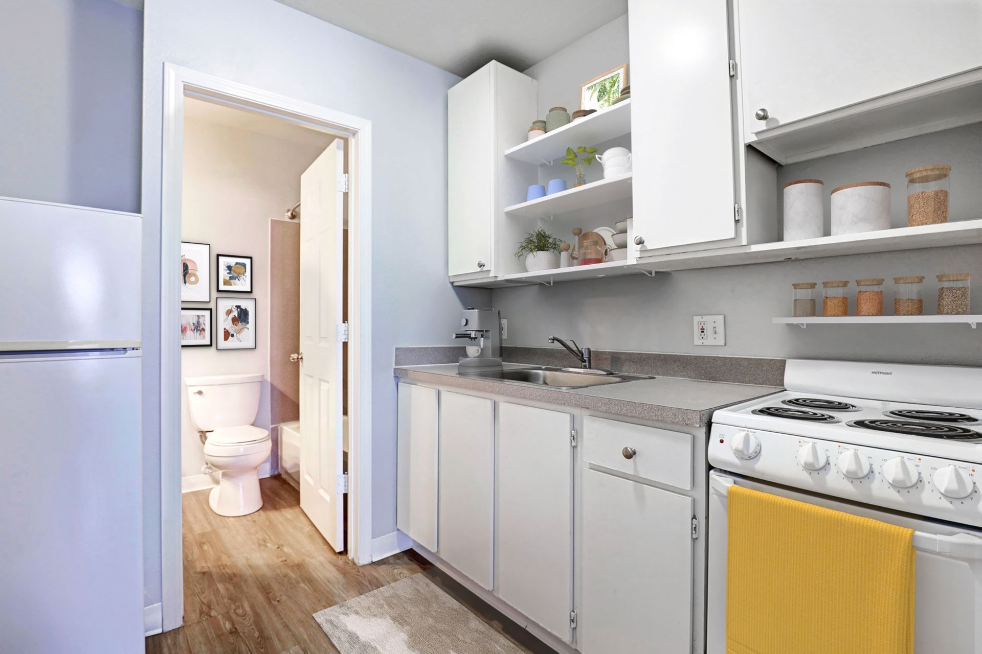 A kitchen with white cabinets , a stove , a refrigerator , a sink and a toilet.