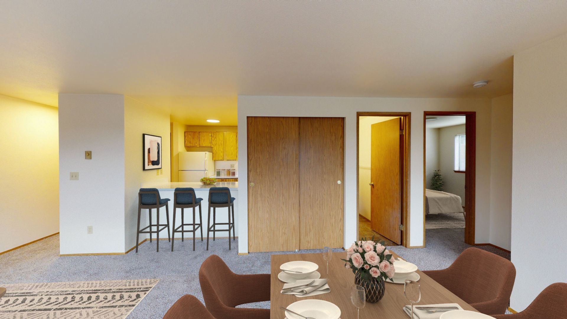 A living room with a dining table and chairs and a kitchen in the background.