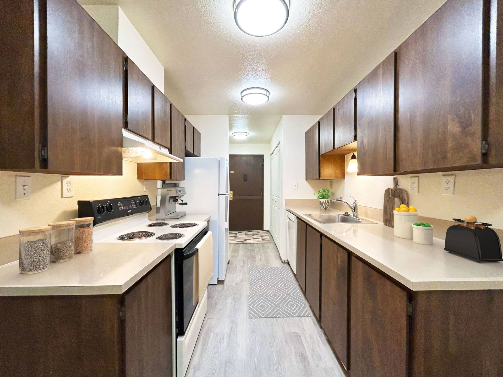 A long kitchen with wooden cabinets and white counter tops.