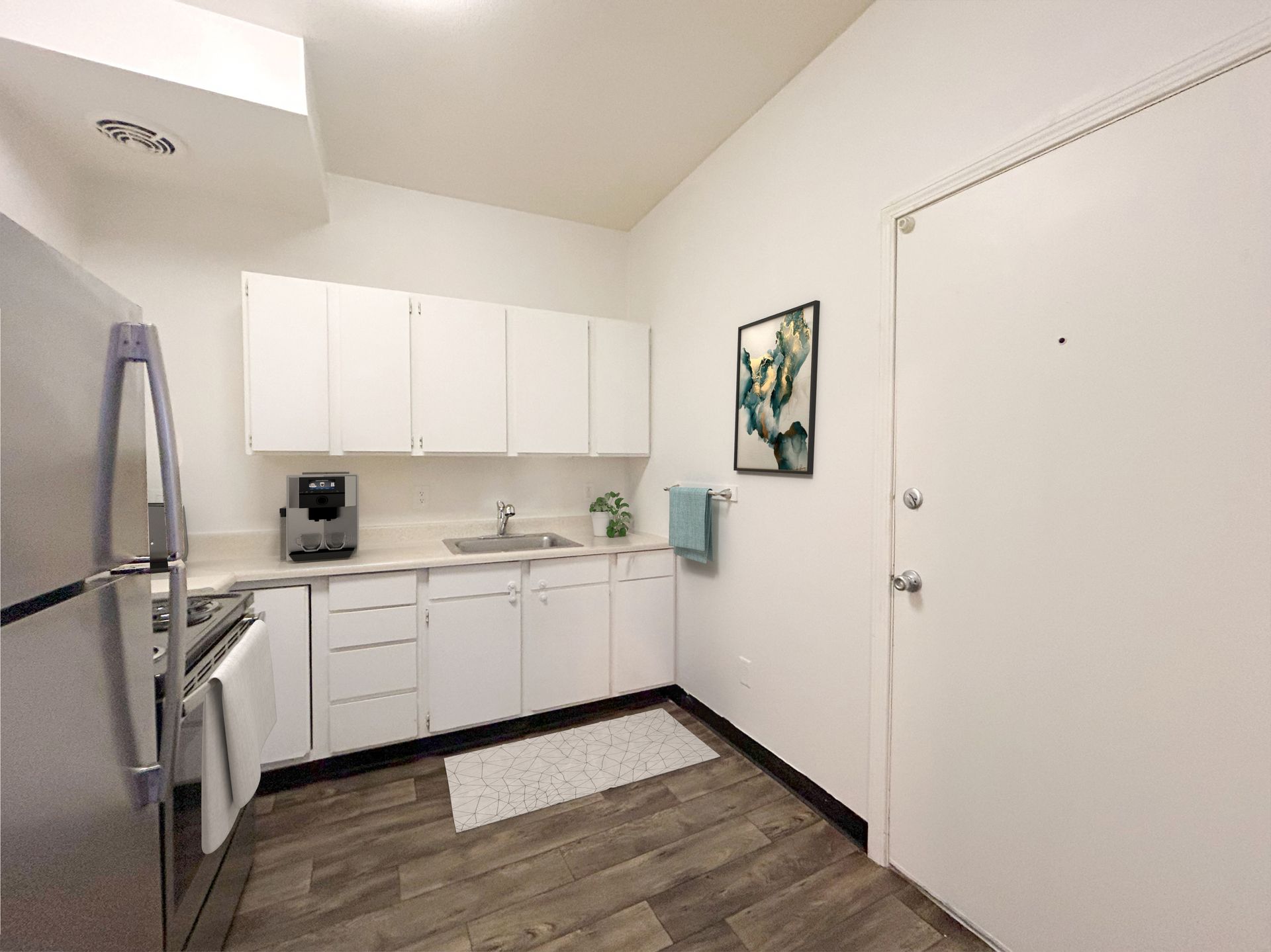 A kitchen with white cabinets , stainless steel appliances , a refrigerator and a sink.
