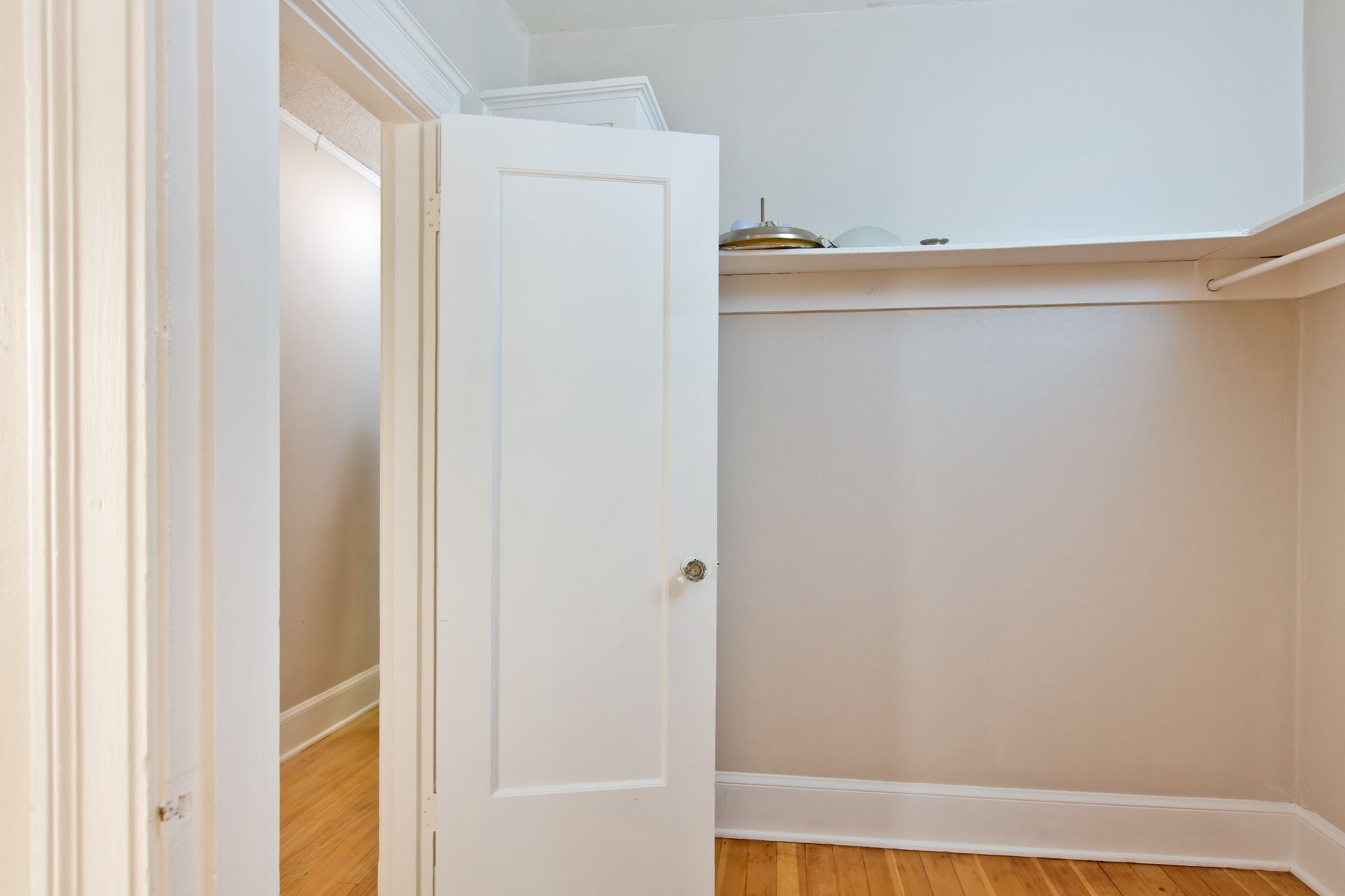 A walk in closet with a white door and a wooden floor