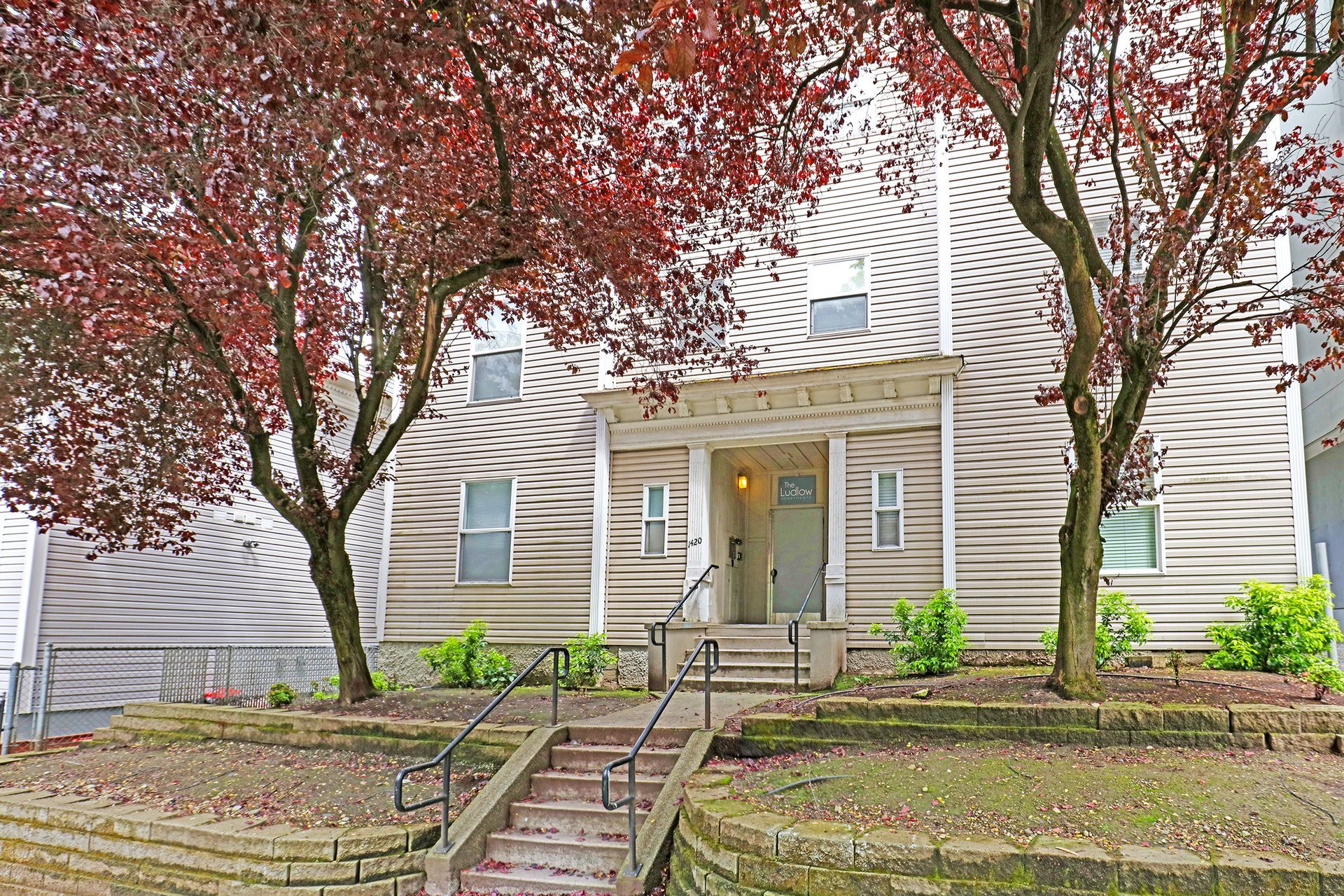 A house with stairs leading up to the front door and trees in front of it.