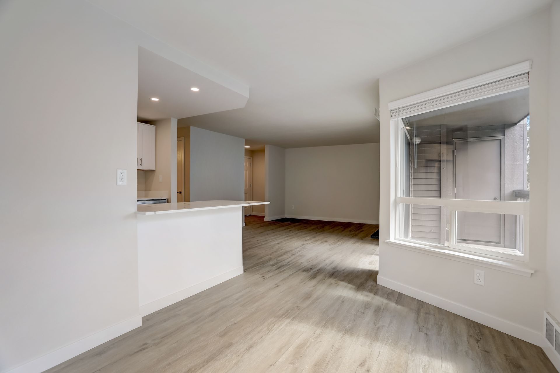 An empty living room with hardwood floors and a large window.