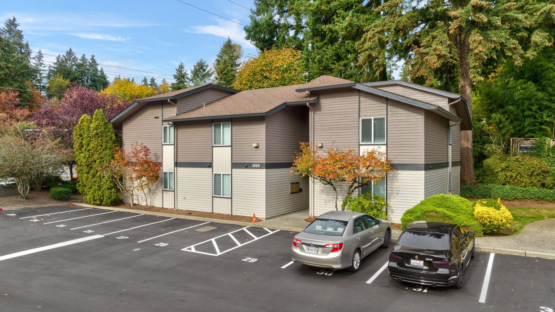 Two cars are parked in front of a large apartment building.