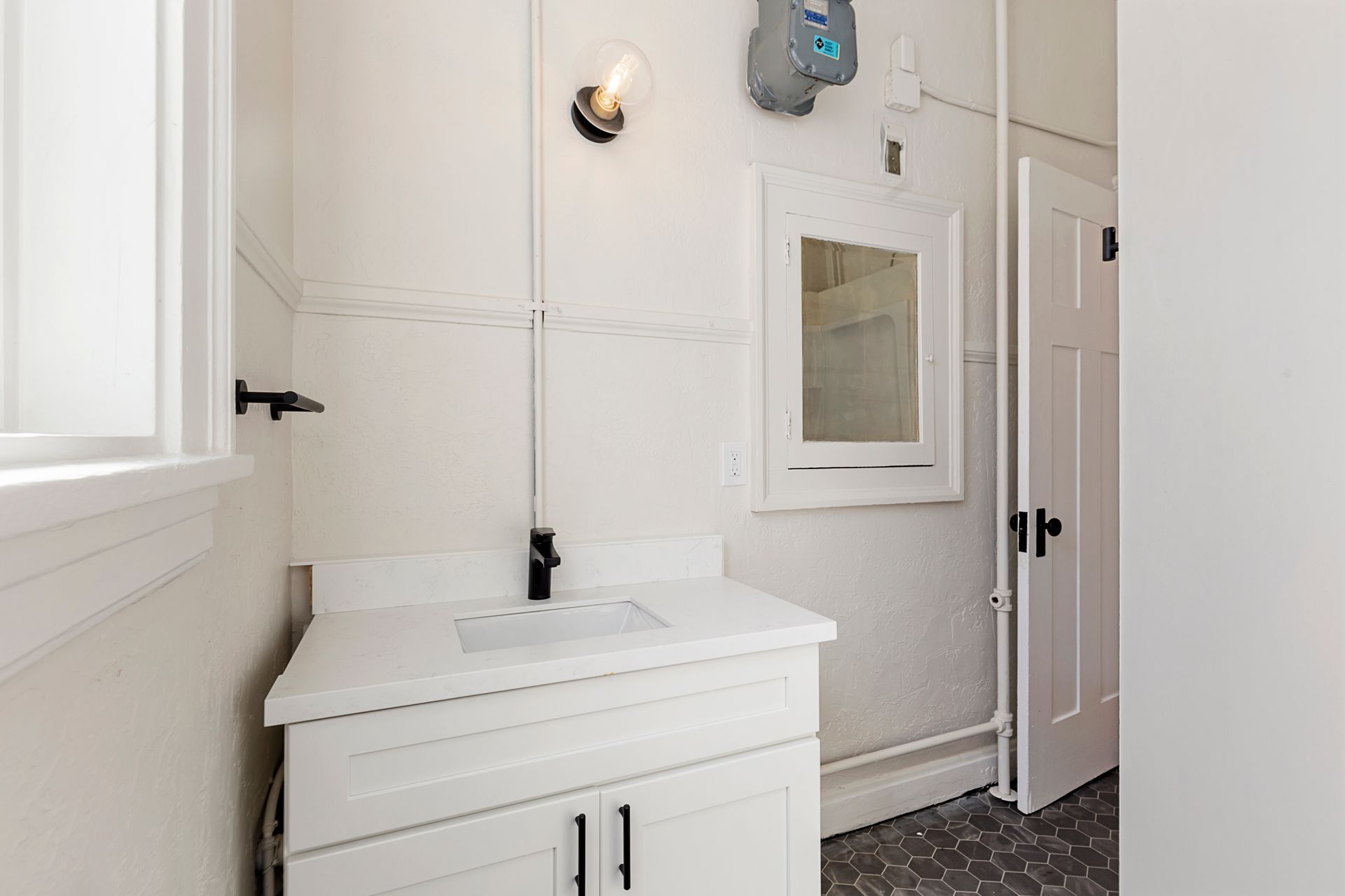 A bathroom with a sink , mirror and window.