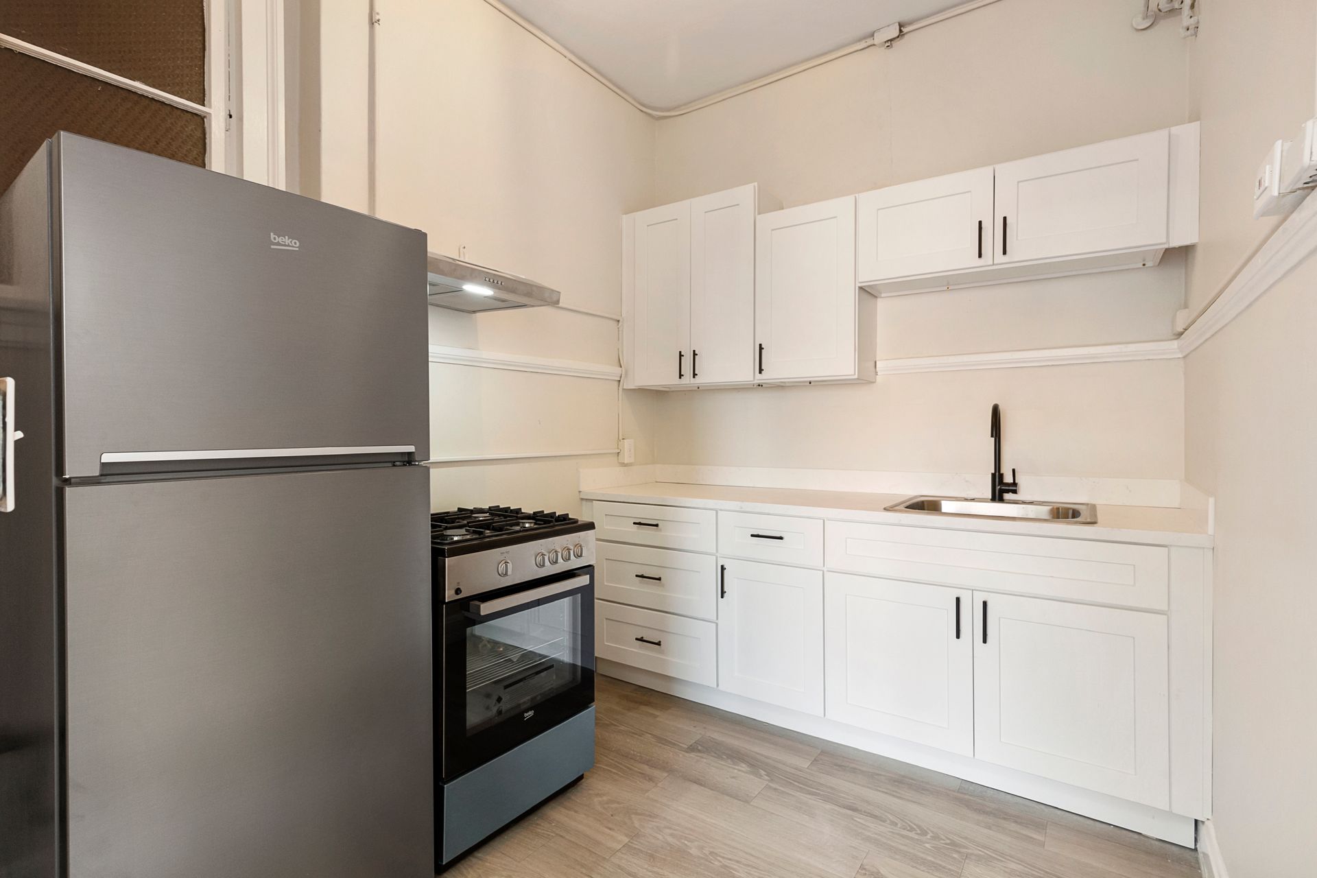 A kitchen with white cabinets , a stove , a refrigerator , and a sink.