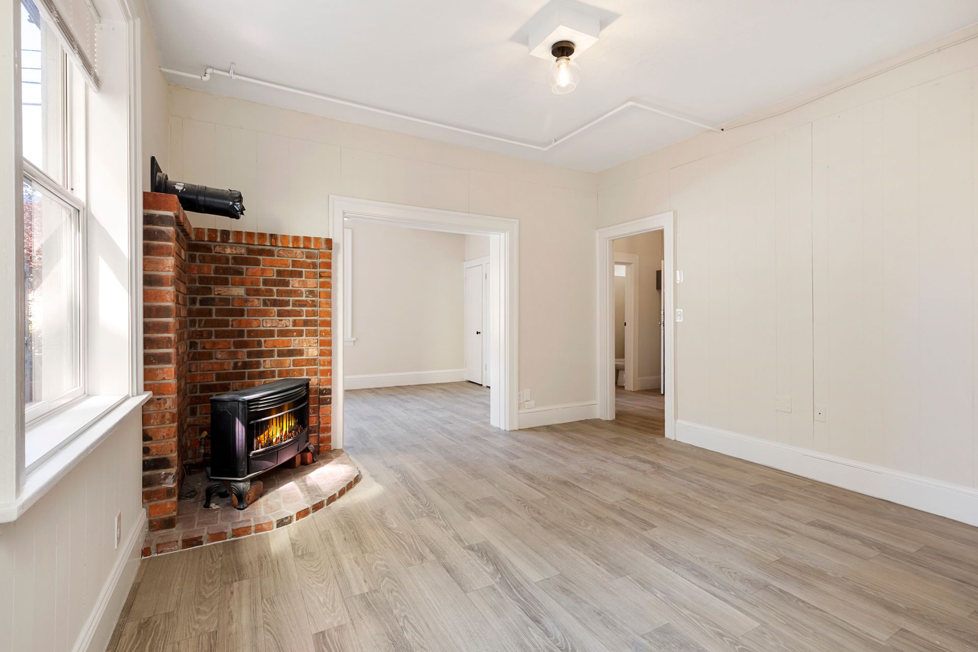 An empty living room with hardwood floors and a brick fireplace.