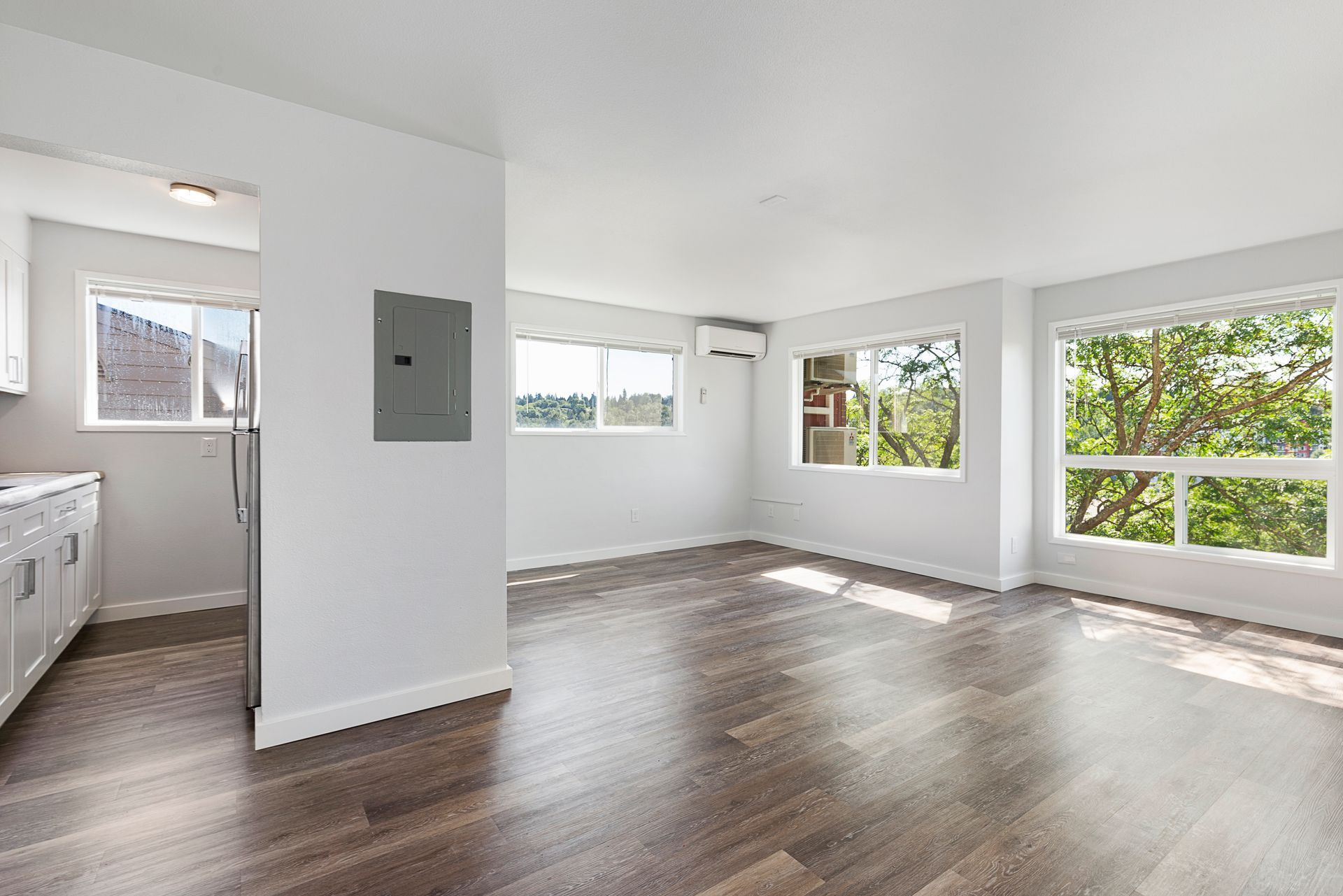 An empty apartment with hardwood floors , white walls , and lots of windows.