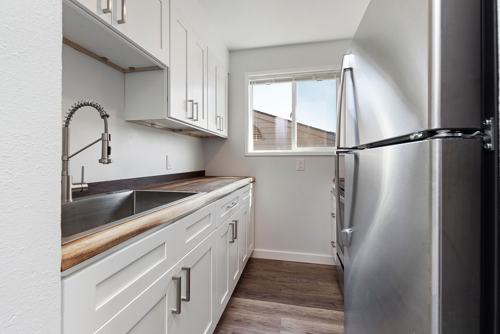 A kitchen with white cabinets , a sink , a refrigerator and a window.