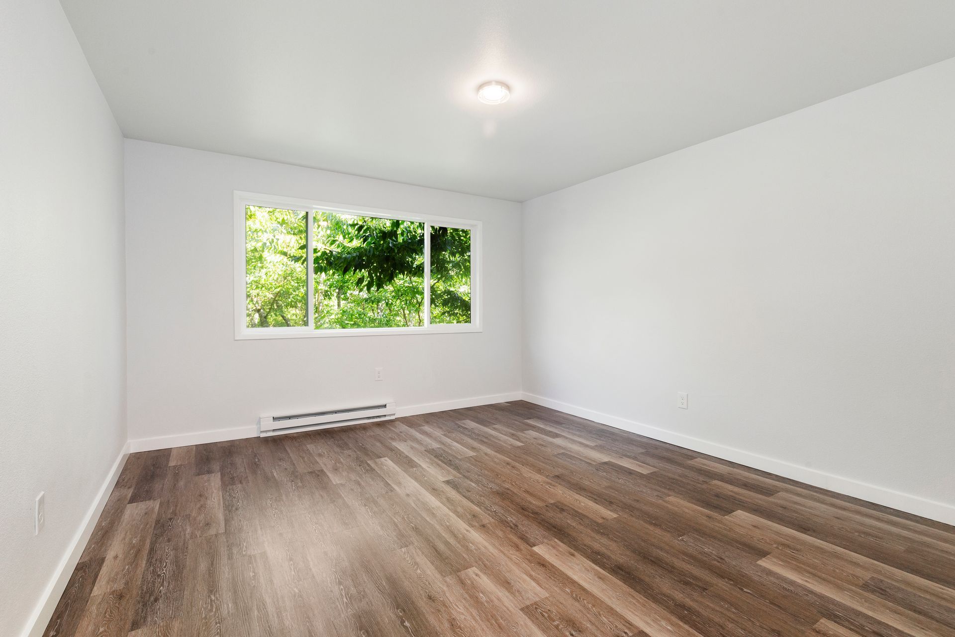 An empty room with hardwood floors and a large window.