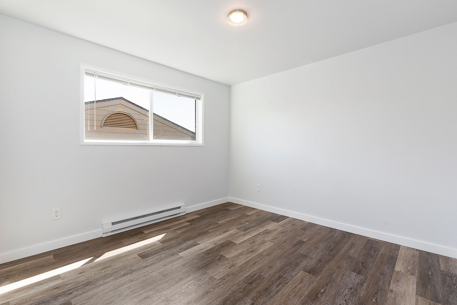 An empty bedroom with hardwood floors and a window.
