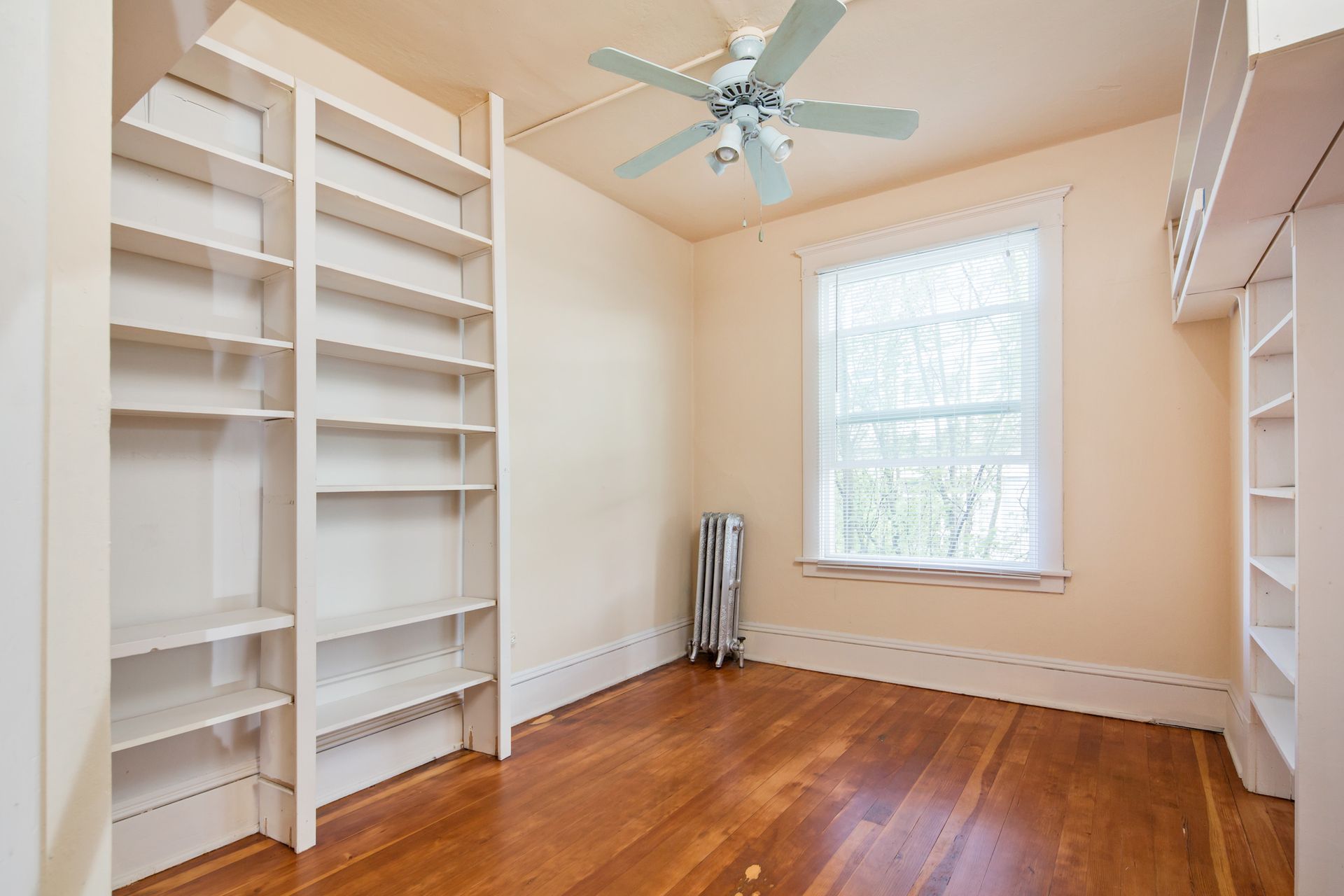 An empty room with a ceiling fan and shelves.