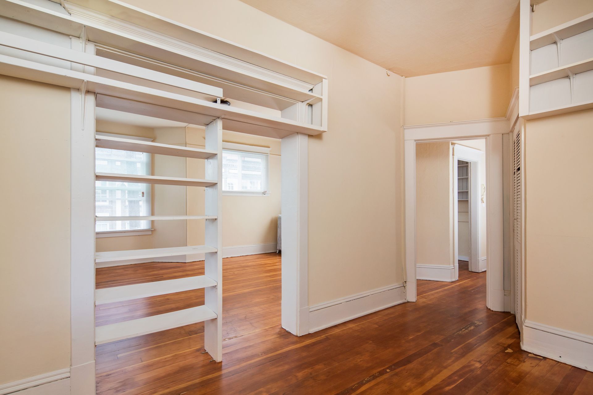 An empty room with hardwood floors and white shelves