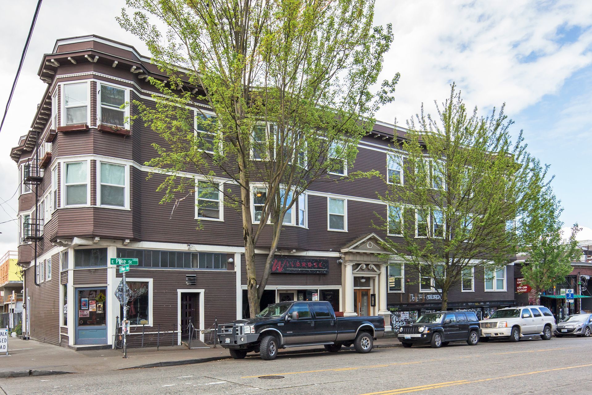 A row of cars are parked in front of a large brown building