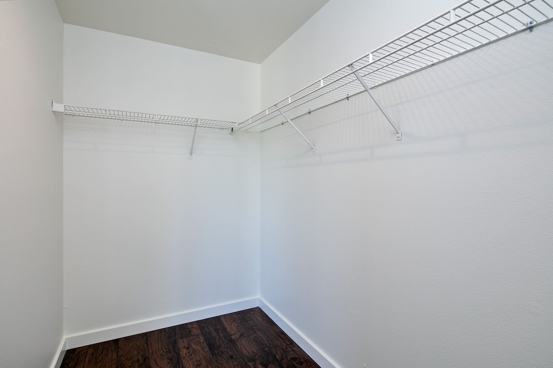 An empty walk in closet with a wire rack and wooden floor.