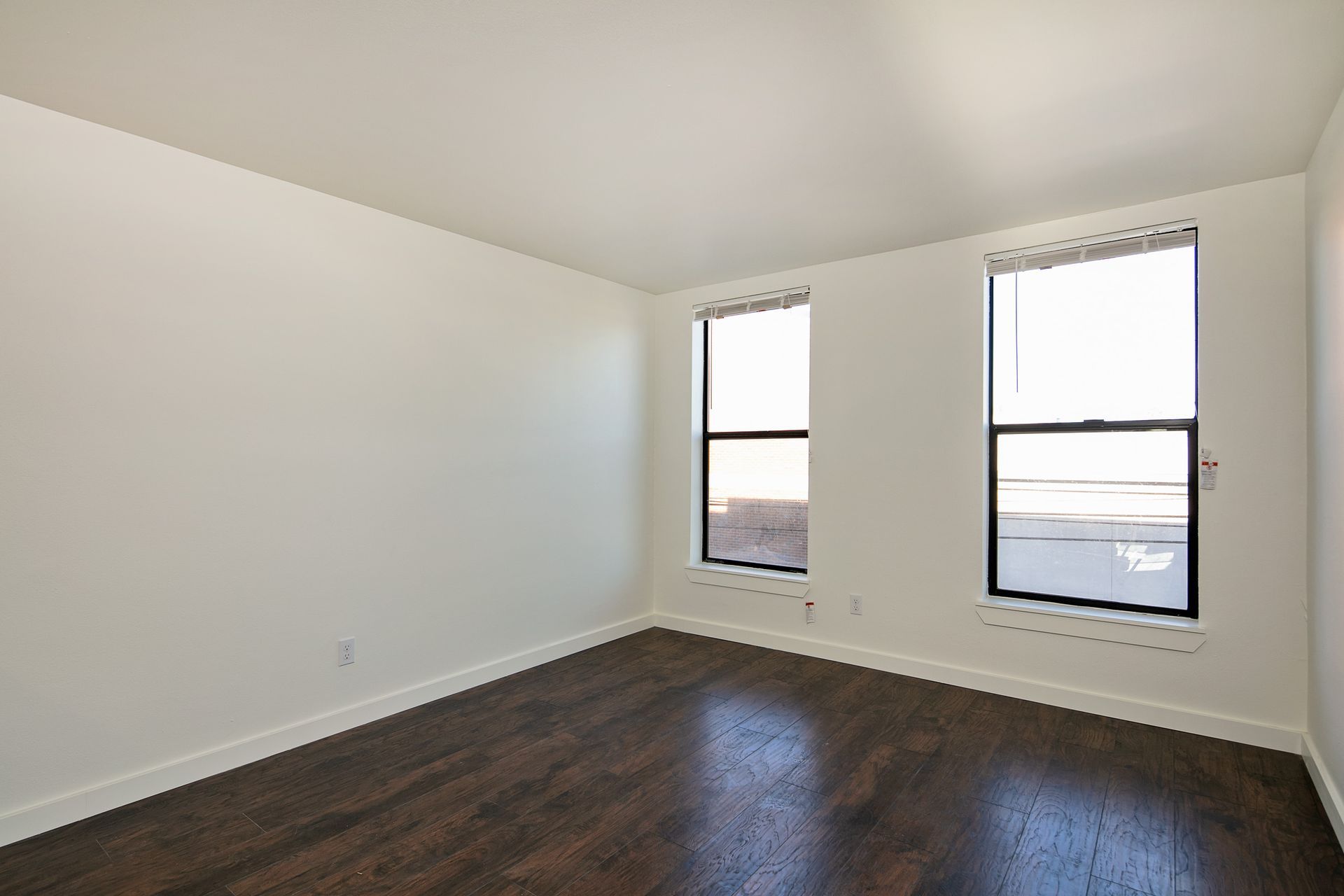 An empty room with two windows and hardwood floors.