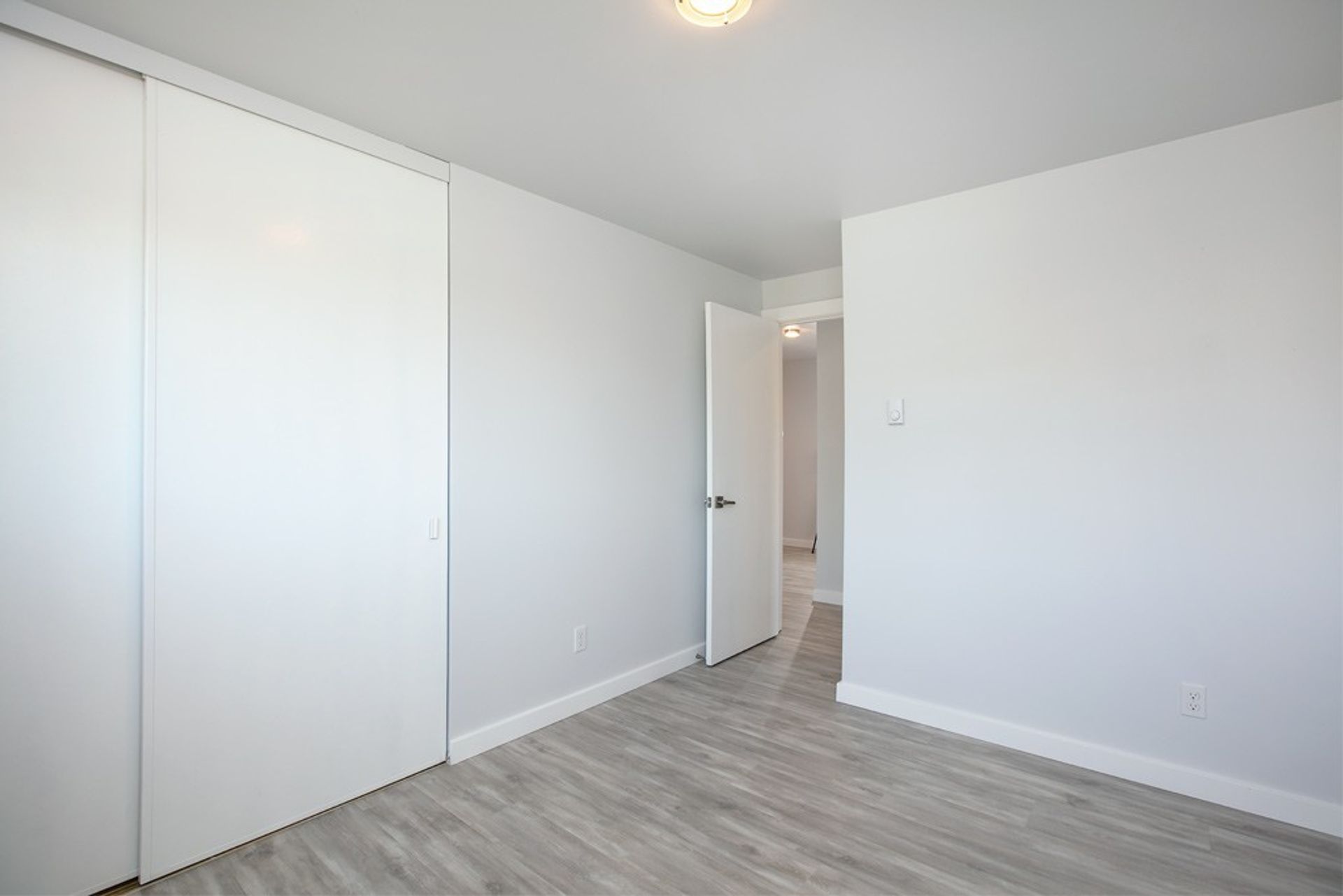 An empty bedroom with hardwood floors and white walls.