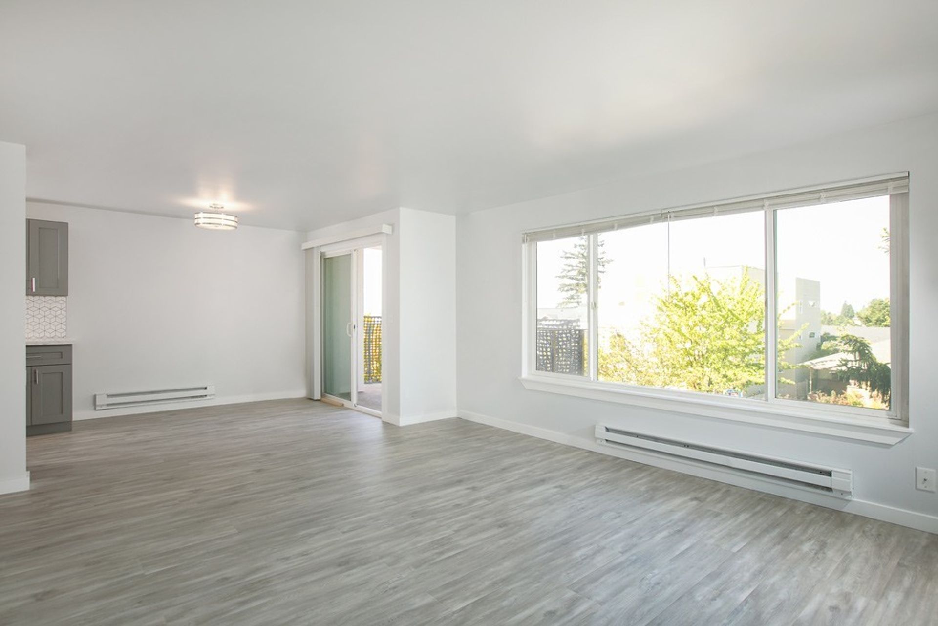 An empty living room with hardwood floors and a large window.
