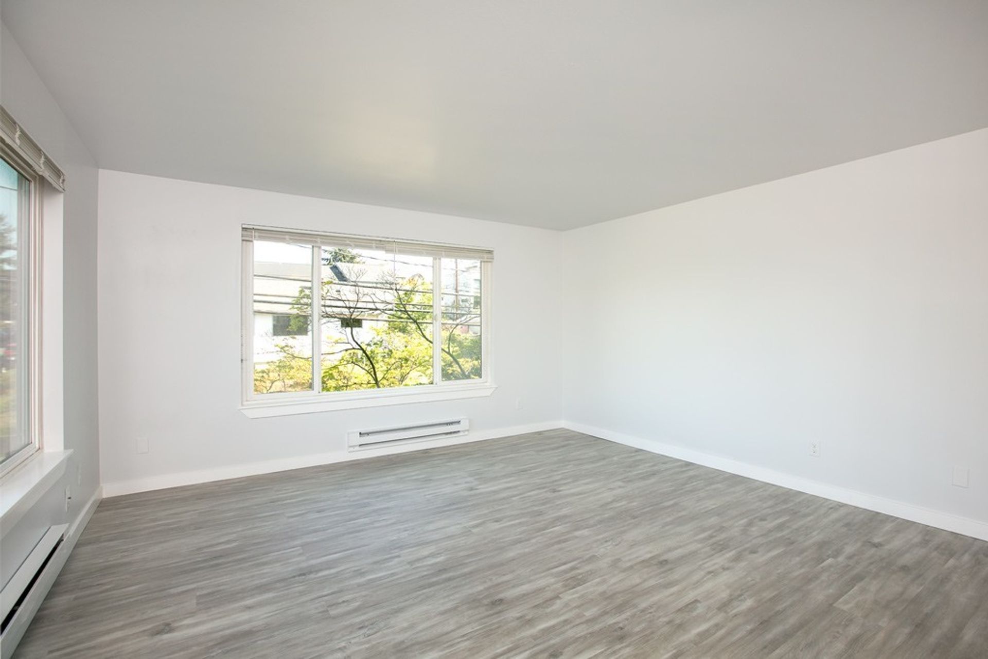 An empty living room with hardwood floors and a large window.