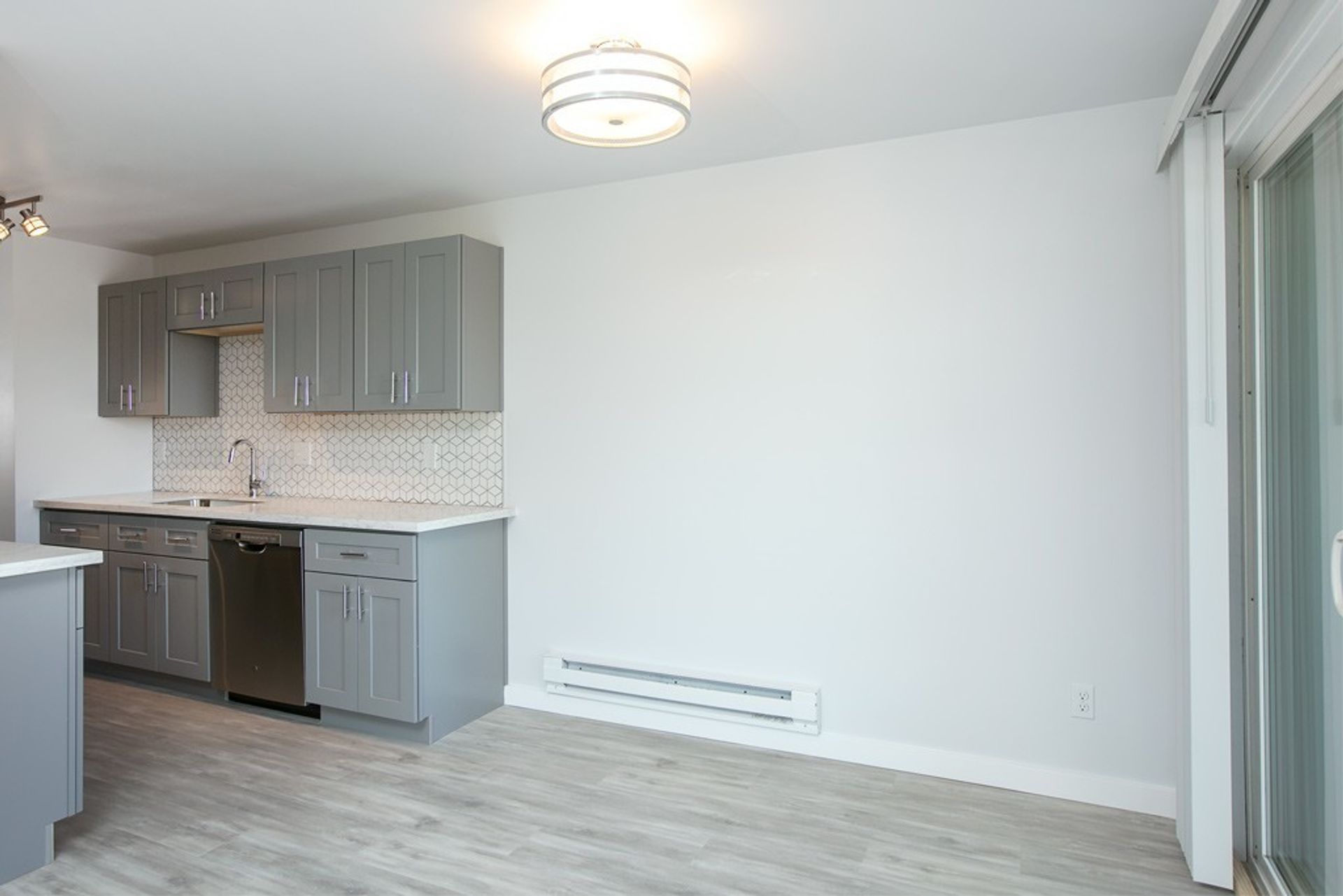 An empty kitchen with gray cabinets and stainless steel appliances.