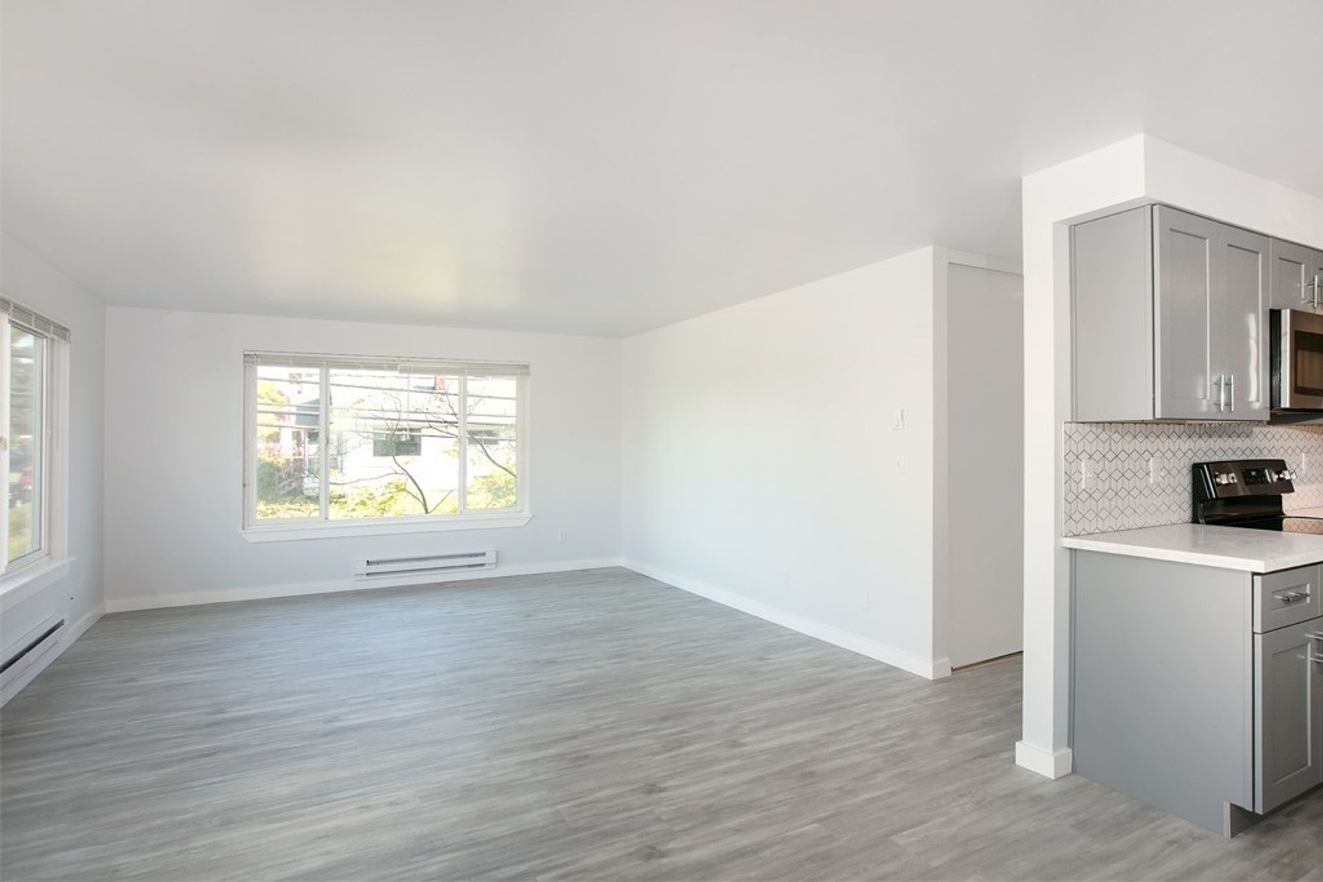 An empty living room with a kitchen in the background.
