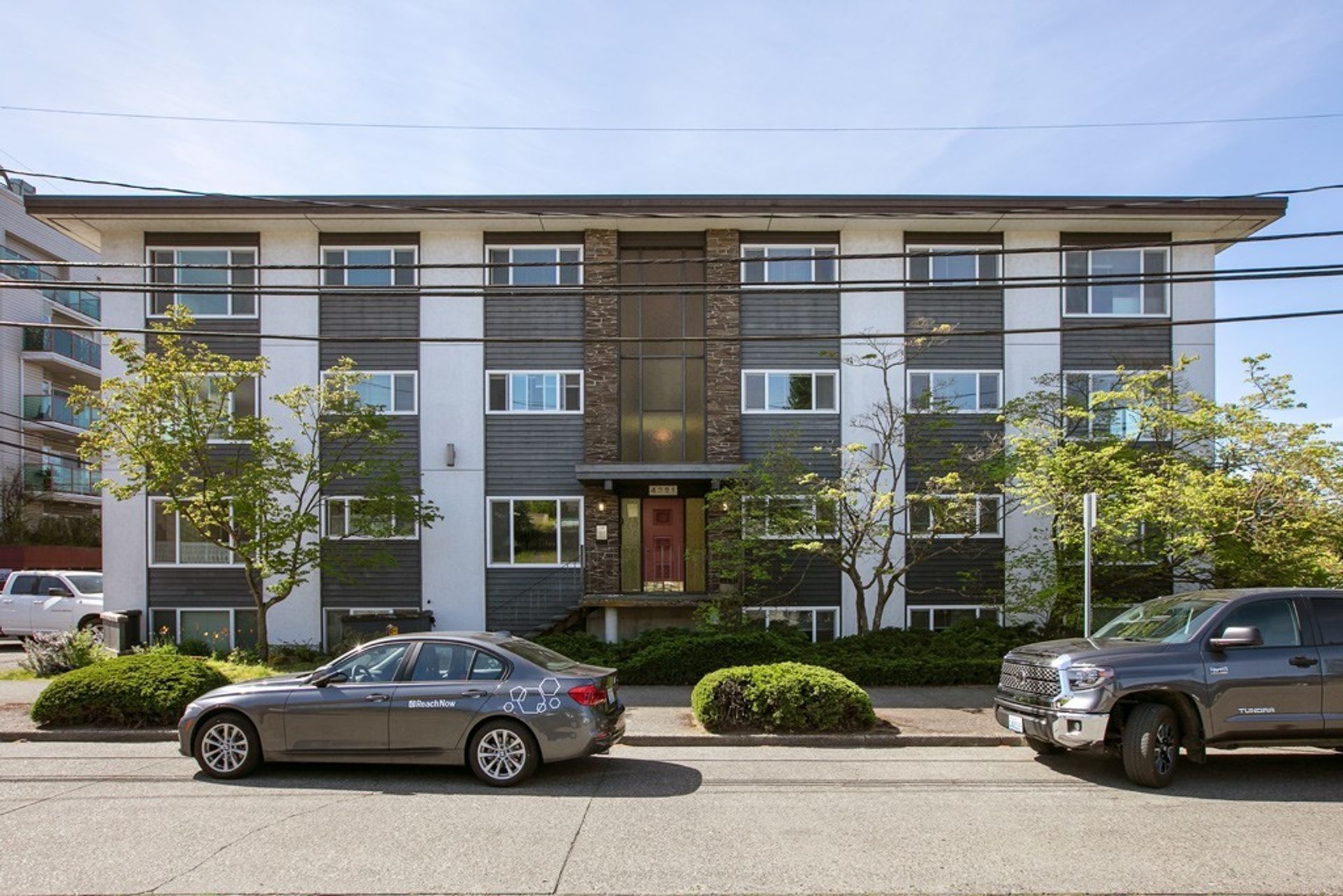 Two cars are parked in front of a large apartment building