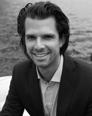 A man in a suit and tie is smiling in a black and white photo.