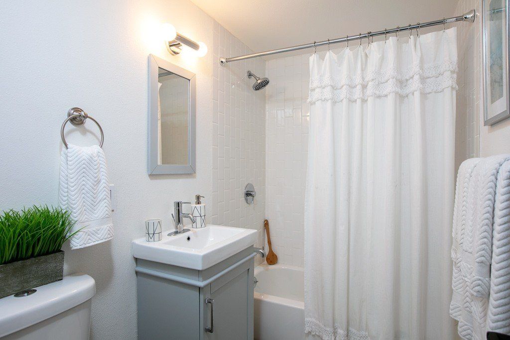 A bathroom with a sink , tub , mirror and shower curtain.
