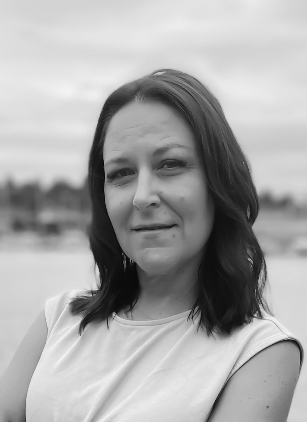 A black and white photo of a woman standing in front of a body of water.