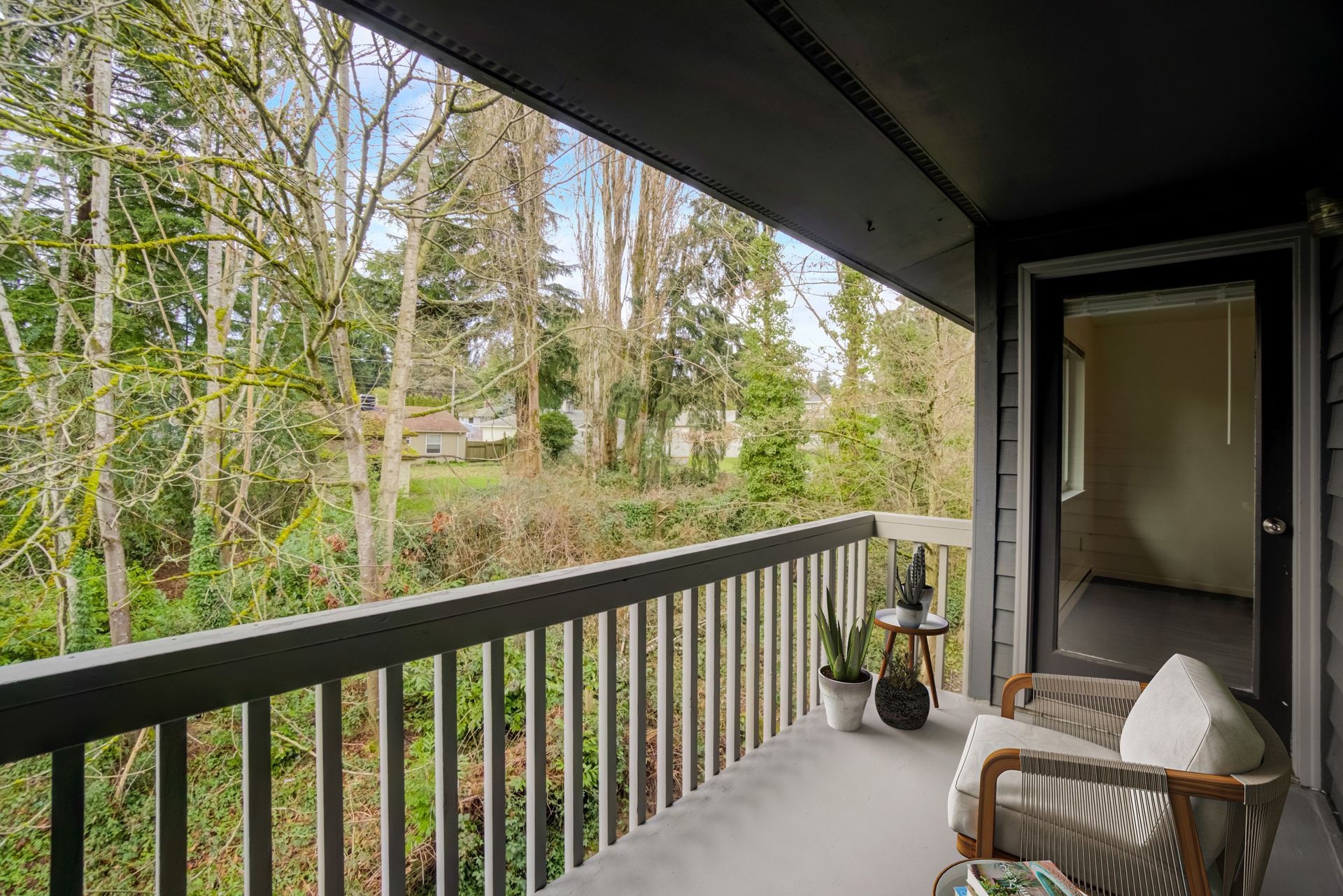 A balcony with a chair and a table overlooking a forest.