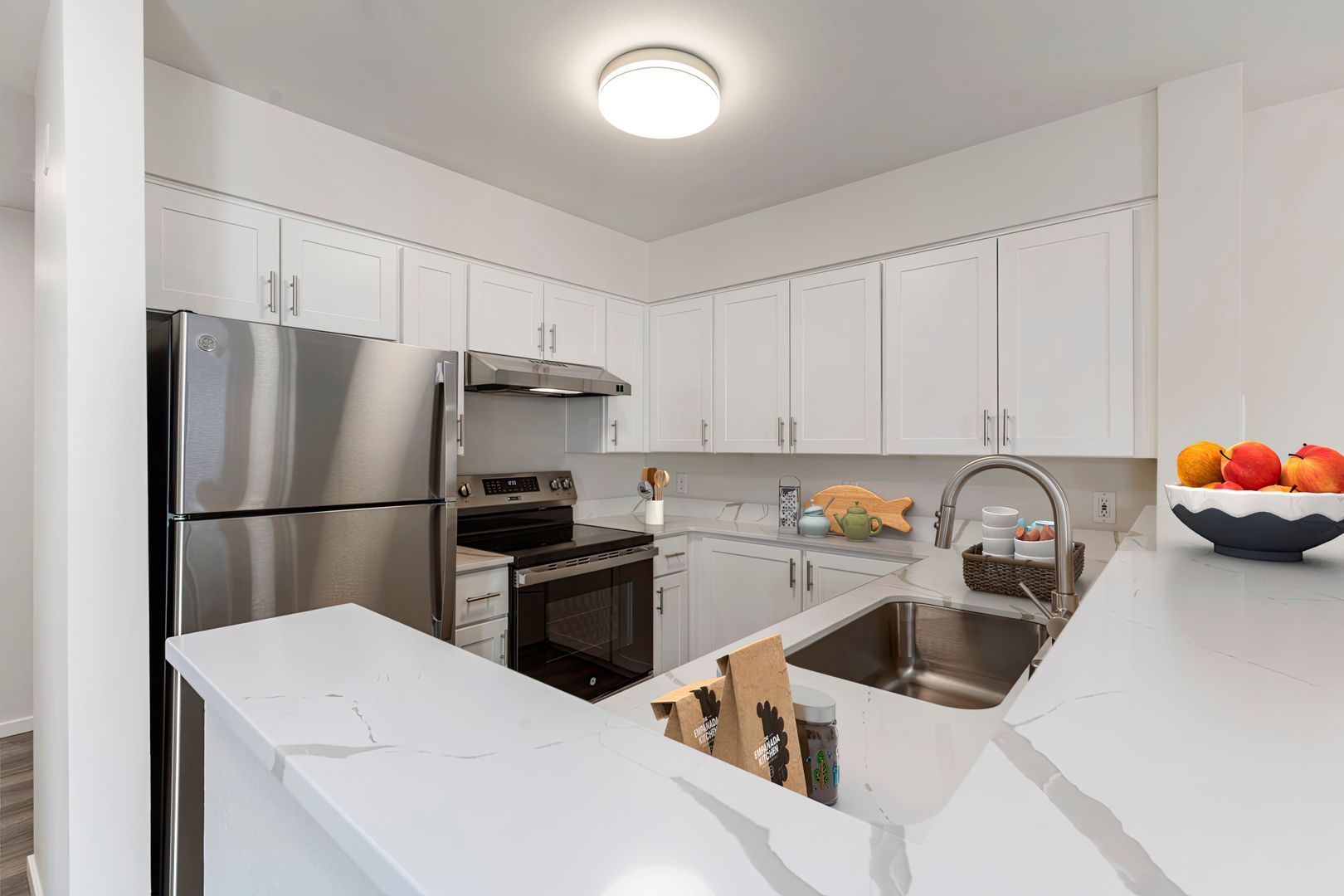 A kitchen with white cabinets , stainless steel appliances , a sink and a refrigerator.