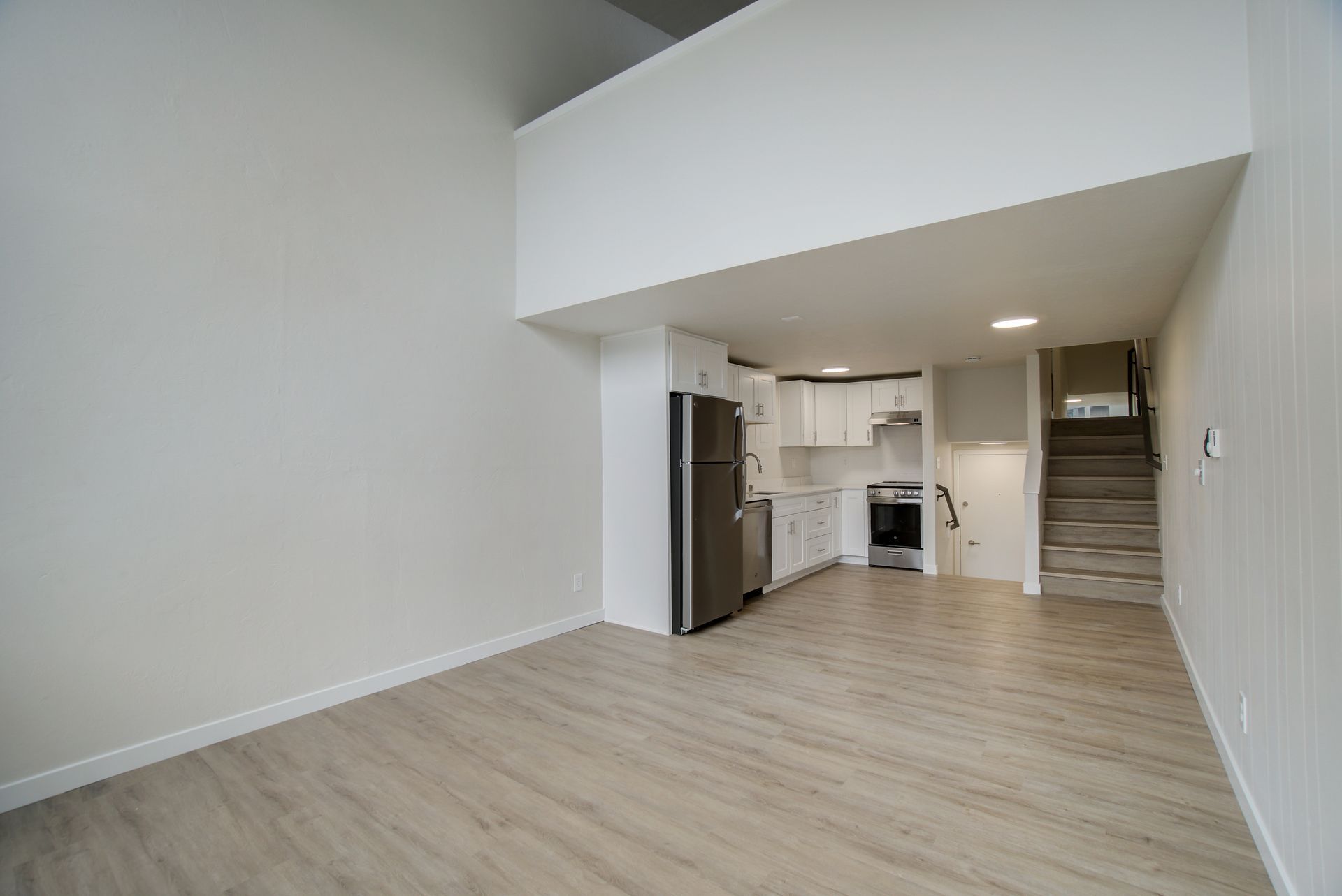 An empty living room with a kitchen and stairs in the background.