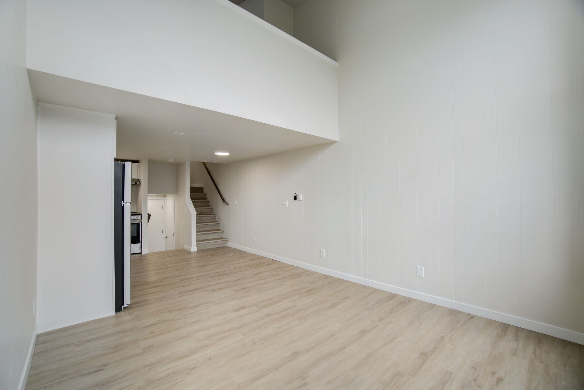 An empty living room with hardwood floors and stairs leading to the second floor.