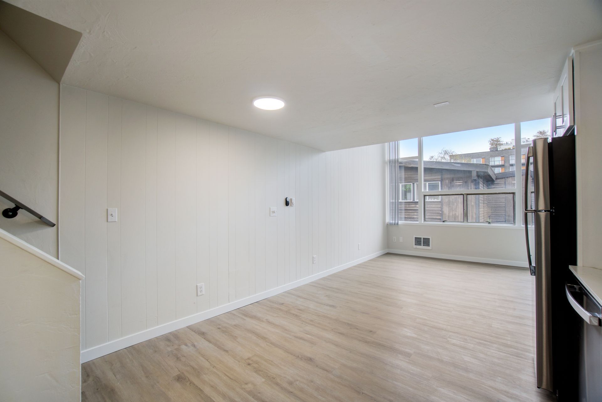 An empty living room with hardwood floors and a large window.