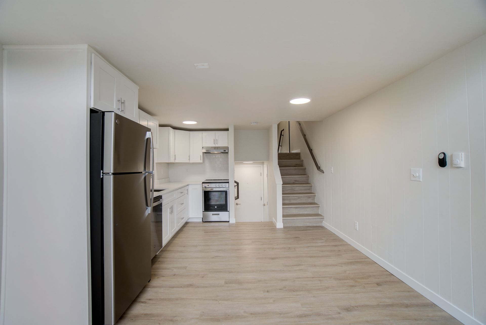 An empty kitchen with a refrigerator , stove , and stairs.