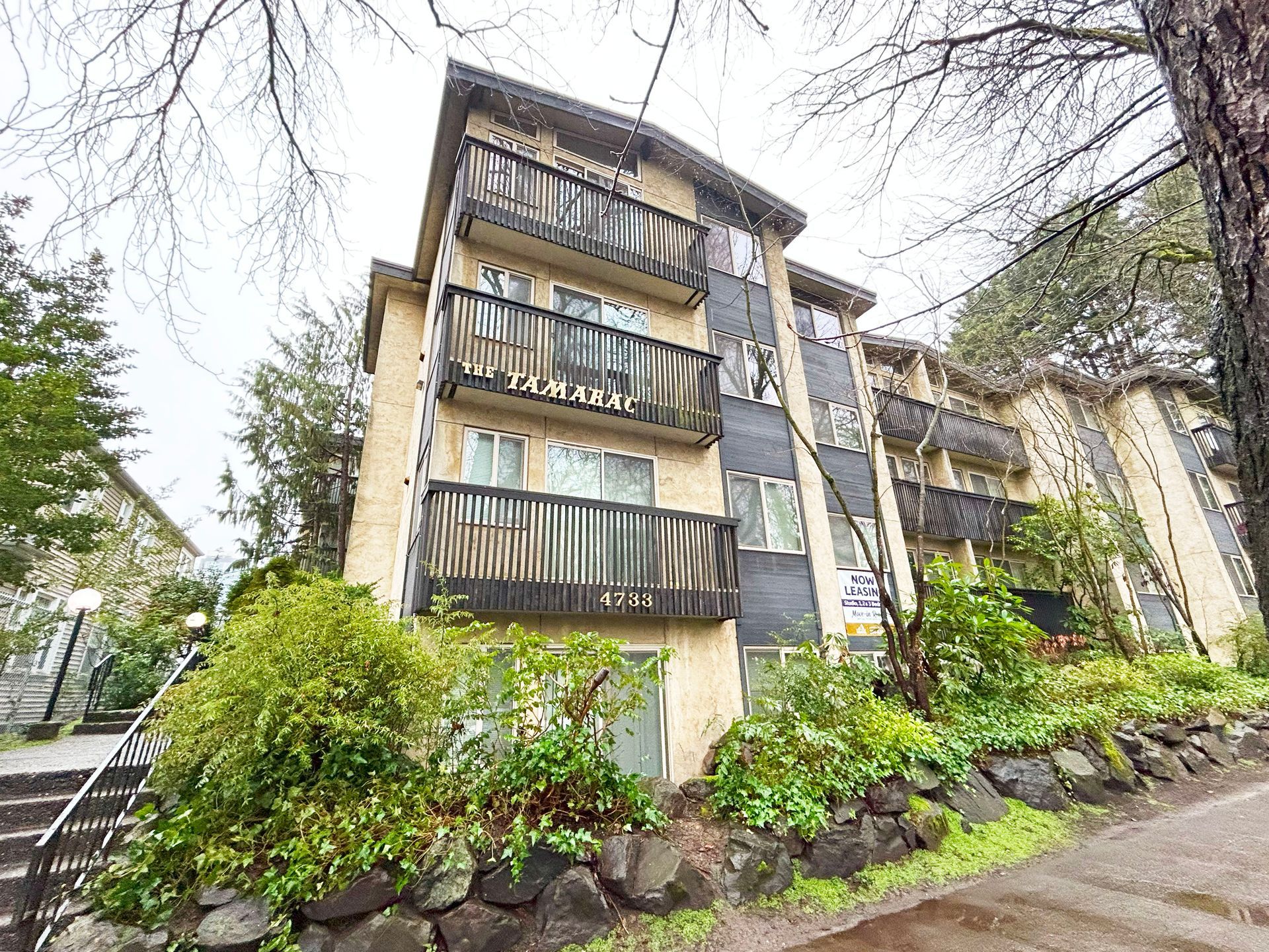 A large apartment building with stairs leading up to it is surrounded by trees and bushes.